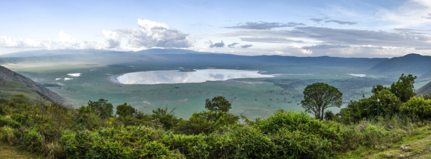 Lush green hills overlooking a lake under a cloudy sky, with a distant volcano in the background