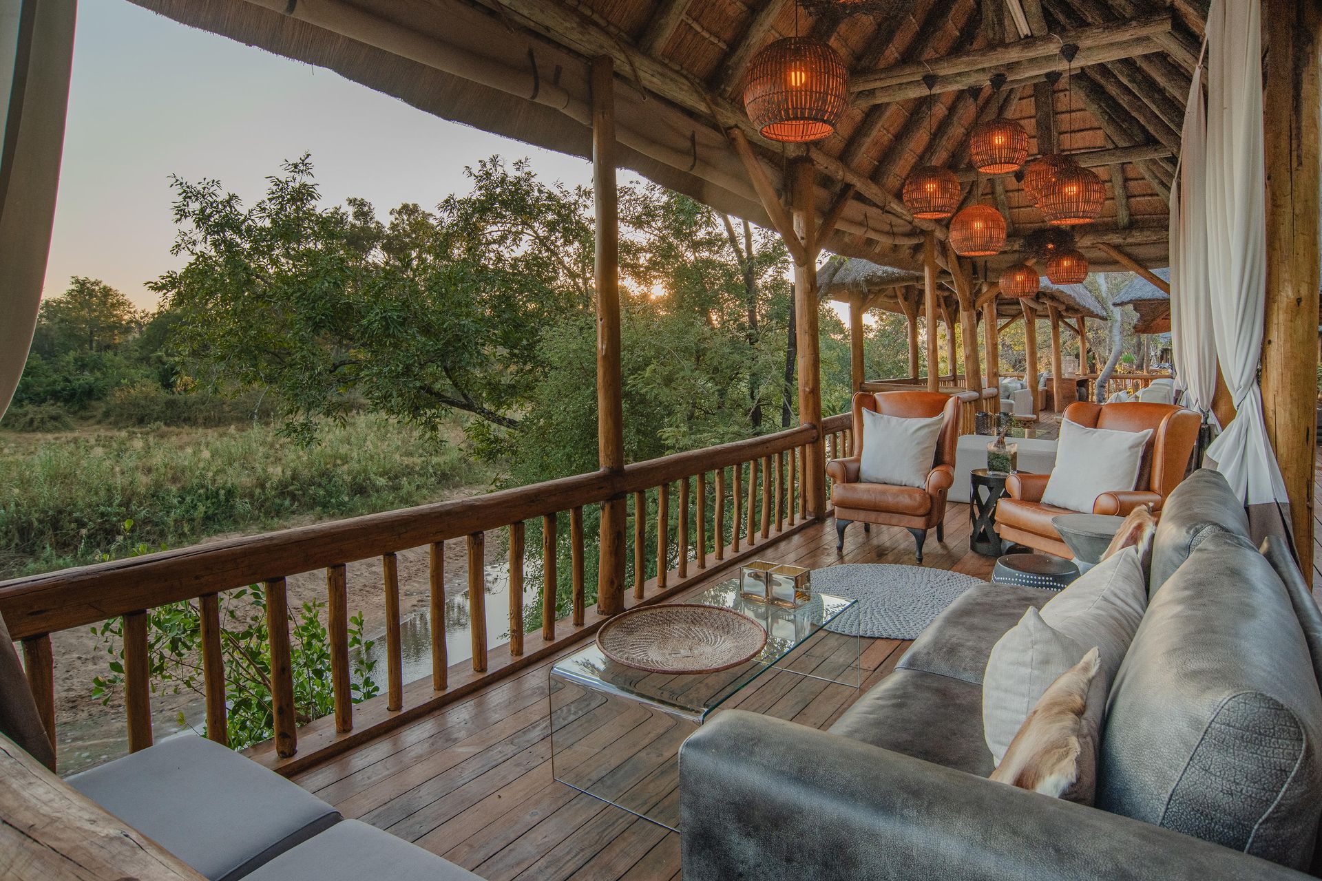Wooden lodge porch with gray sofas, lanterns, and river views at sunset