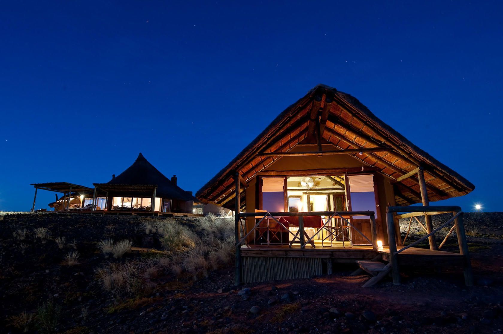 A small house with a thatched roof is lit up at night Namibia Safari