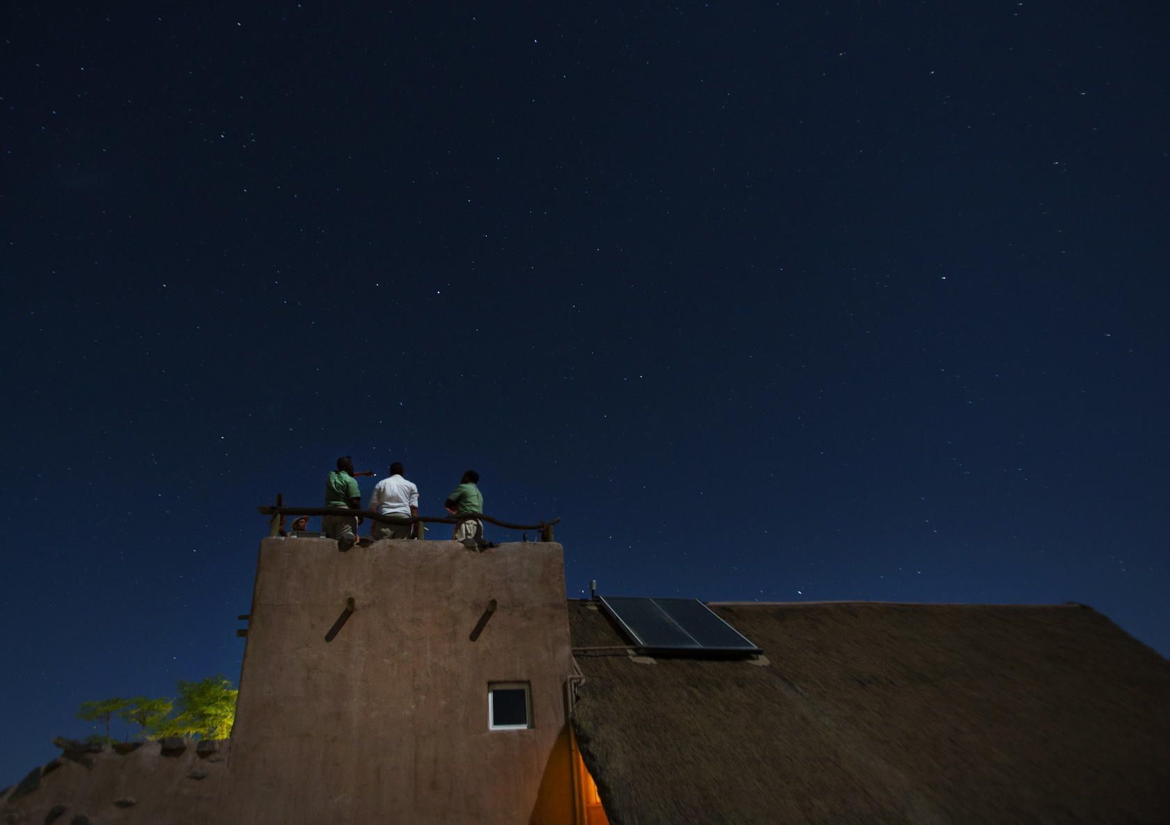 Two people are sitting on the roof of a building looking at the stars. Namibia Safari