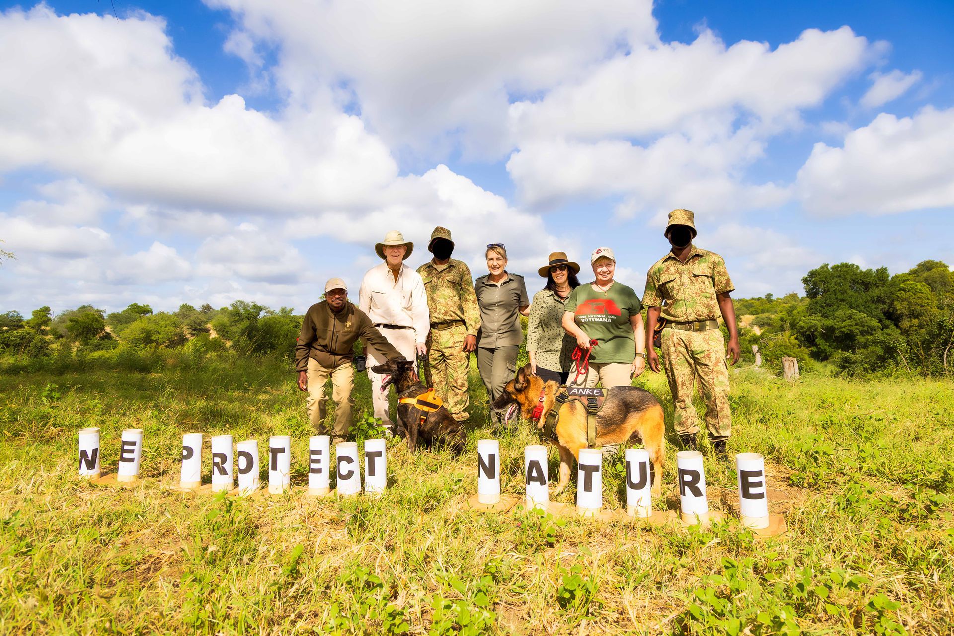 A group of people and dogs stands in a field with a sign that reads 