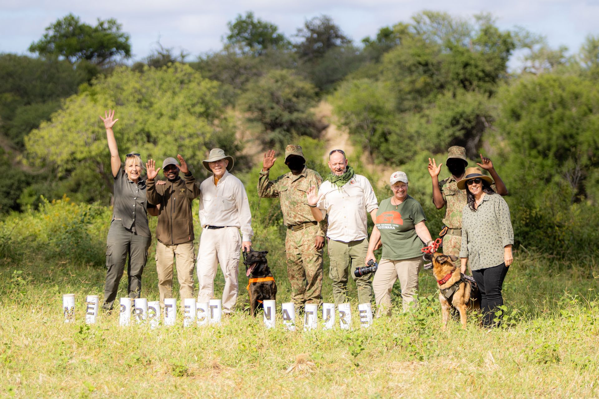 Group of Martin Meyer Safari guests stands in the field with a K9 unit, with a