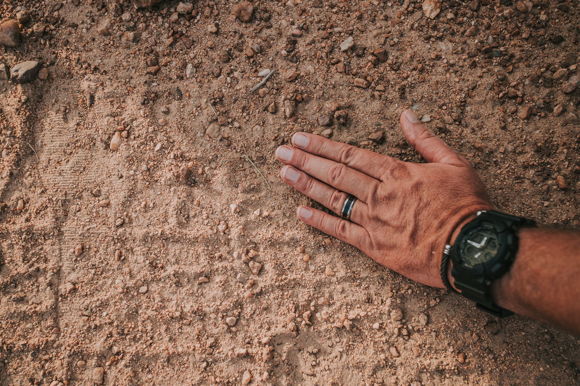 A person wearing a watch is laying their hand on a pile of dirt.
