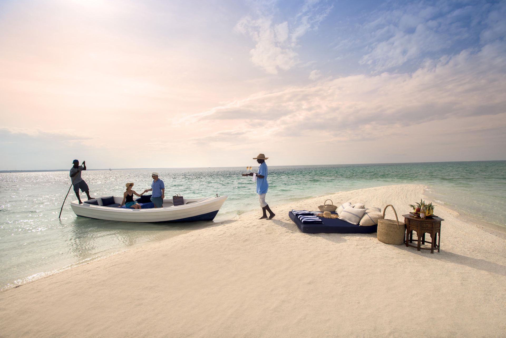 People on a sandbar with a boat and picnic setup under a blue sky.