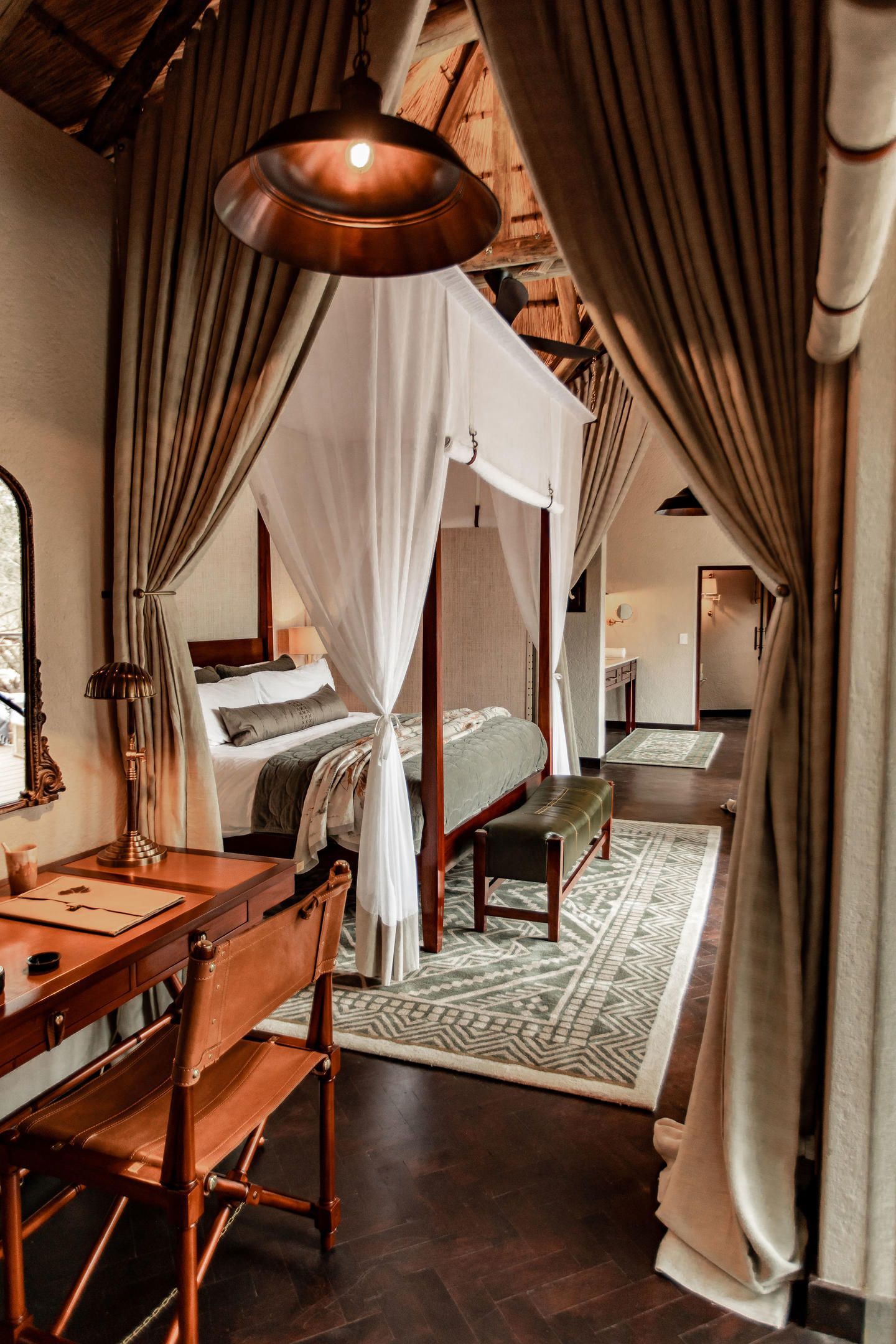 A bedroom with a canopy bed , a desk , chairs and a mirror.