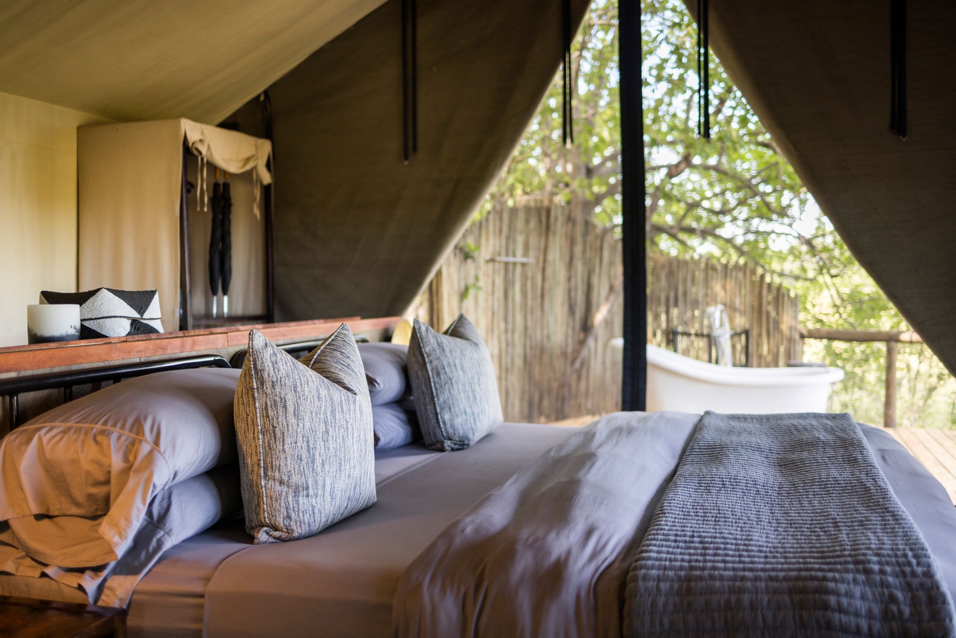 Bedroom in a luxury tent overlooking a deck with a bathtub and trees.