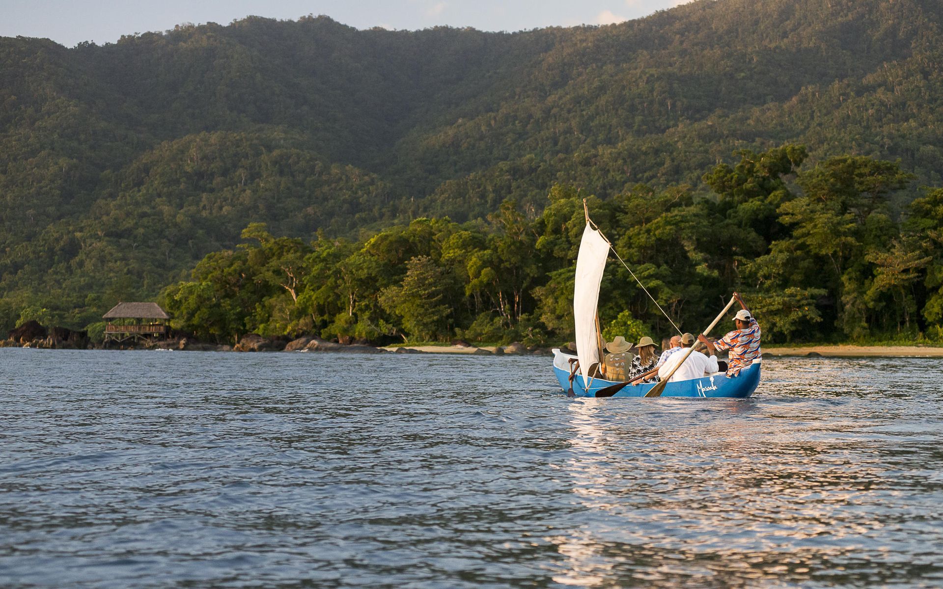 Sailboat on water near lush green shore. Mountains in the background.