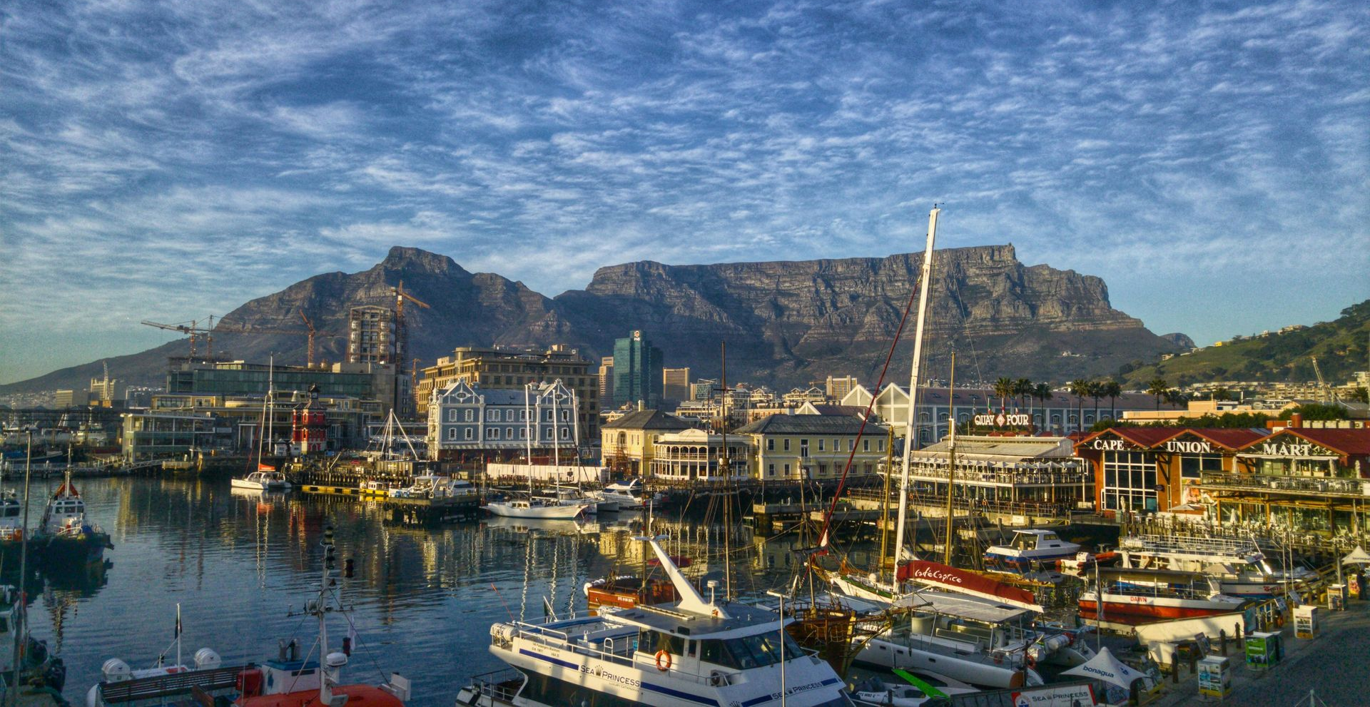 Harbor view with boats, buildings, and Table Mountain under a cloudy sky.