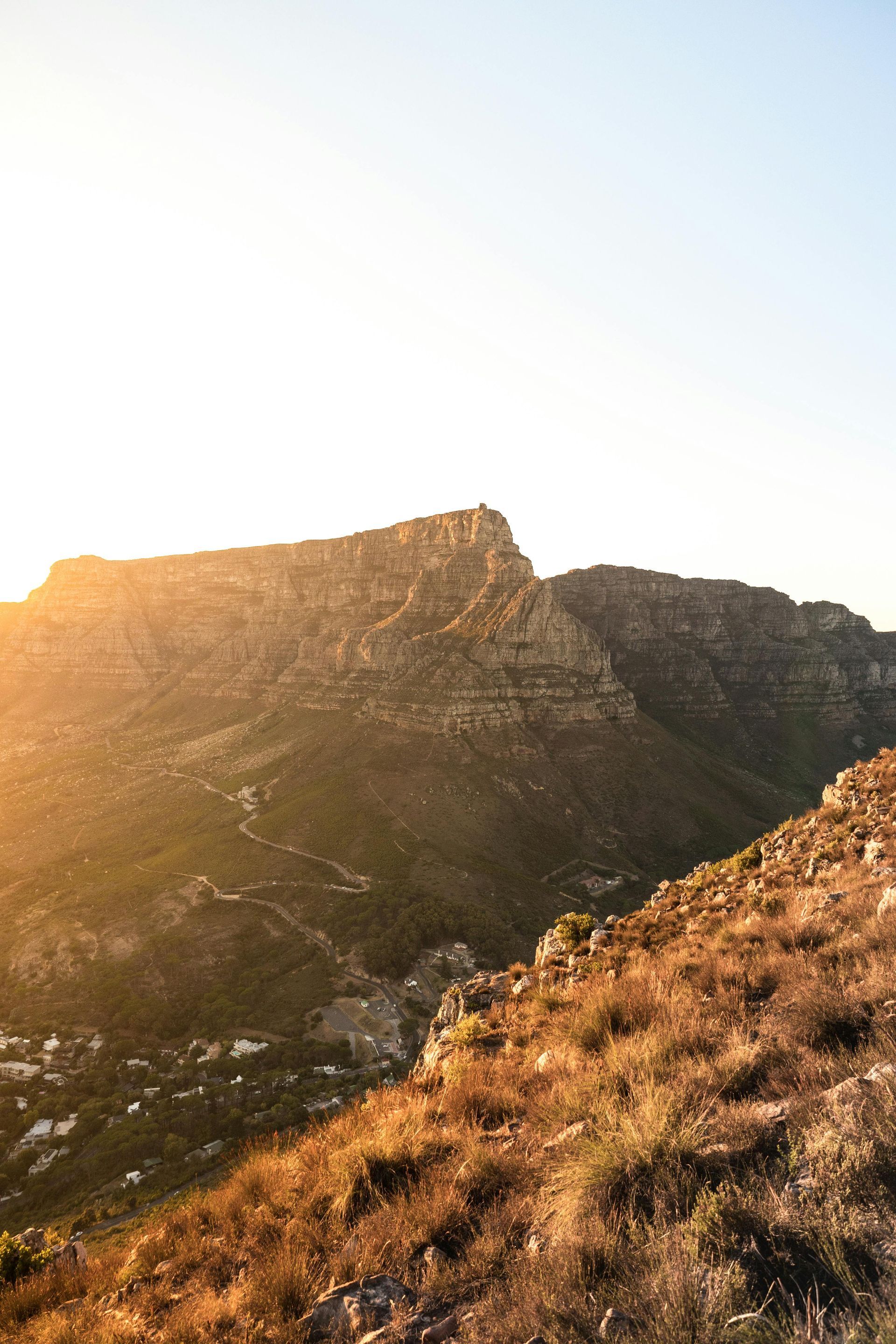 Mountain ridge at sunset, with golden light illuminating the rugged terrain and dry grass in the foreground.