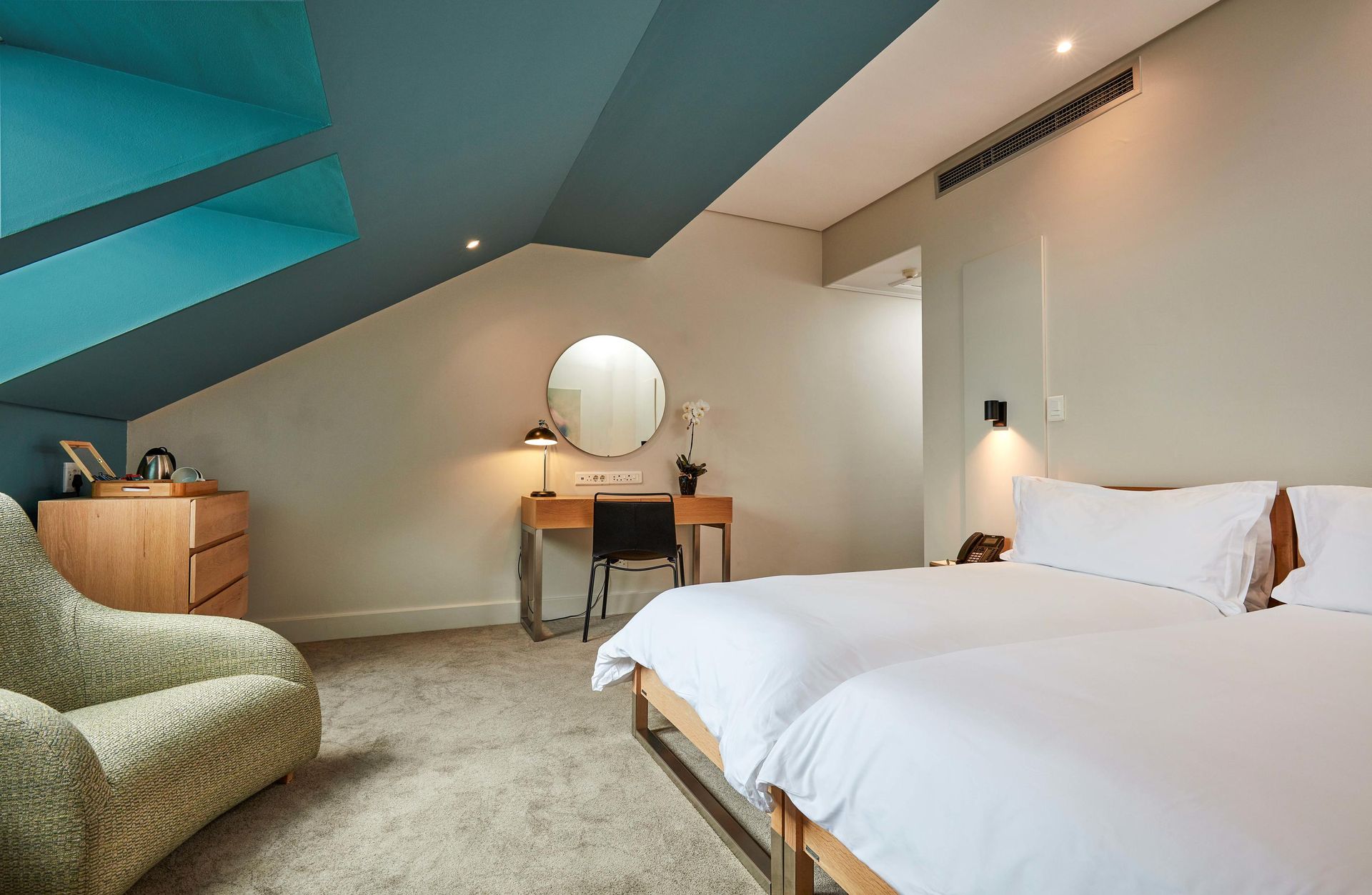 Cozy attic bedroom with white bed, desk, round mirror, and teal accent ceiling