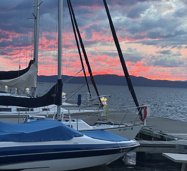 Fiery red and pink sunset sky behind sailboat masts and furled sails at a marina