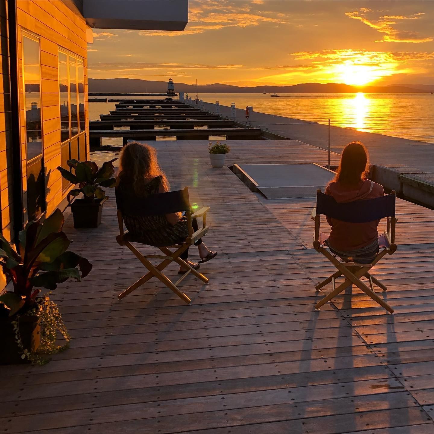 Two guests in director’s chairs on a waterfront deck watching the sunset over the lake and docks