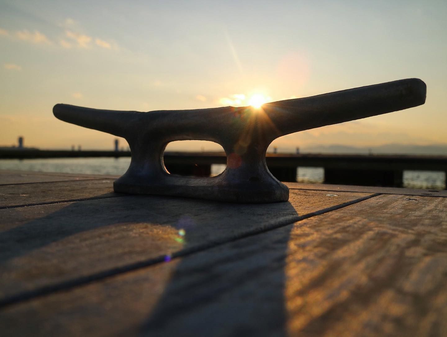 Close-up of a dock cleat silhouetted against the setting sun on a wooden dock