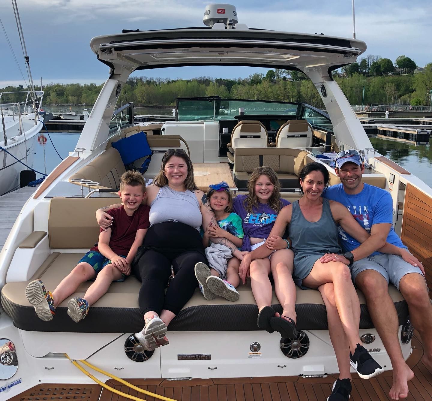 Group of adults and children smiling together on the seating of a motor yacht docked at a marina