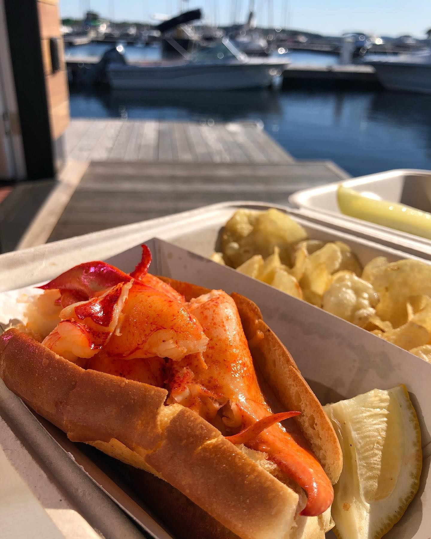 Takeout containers of fried food on a dock-side table, with boats moored on the water behind