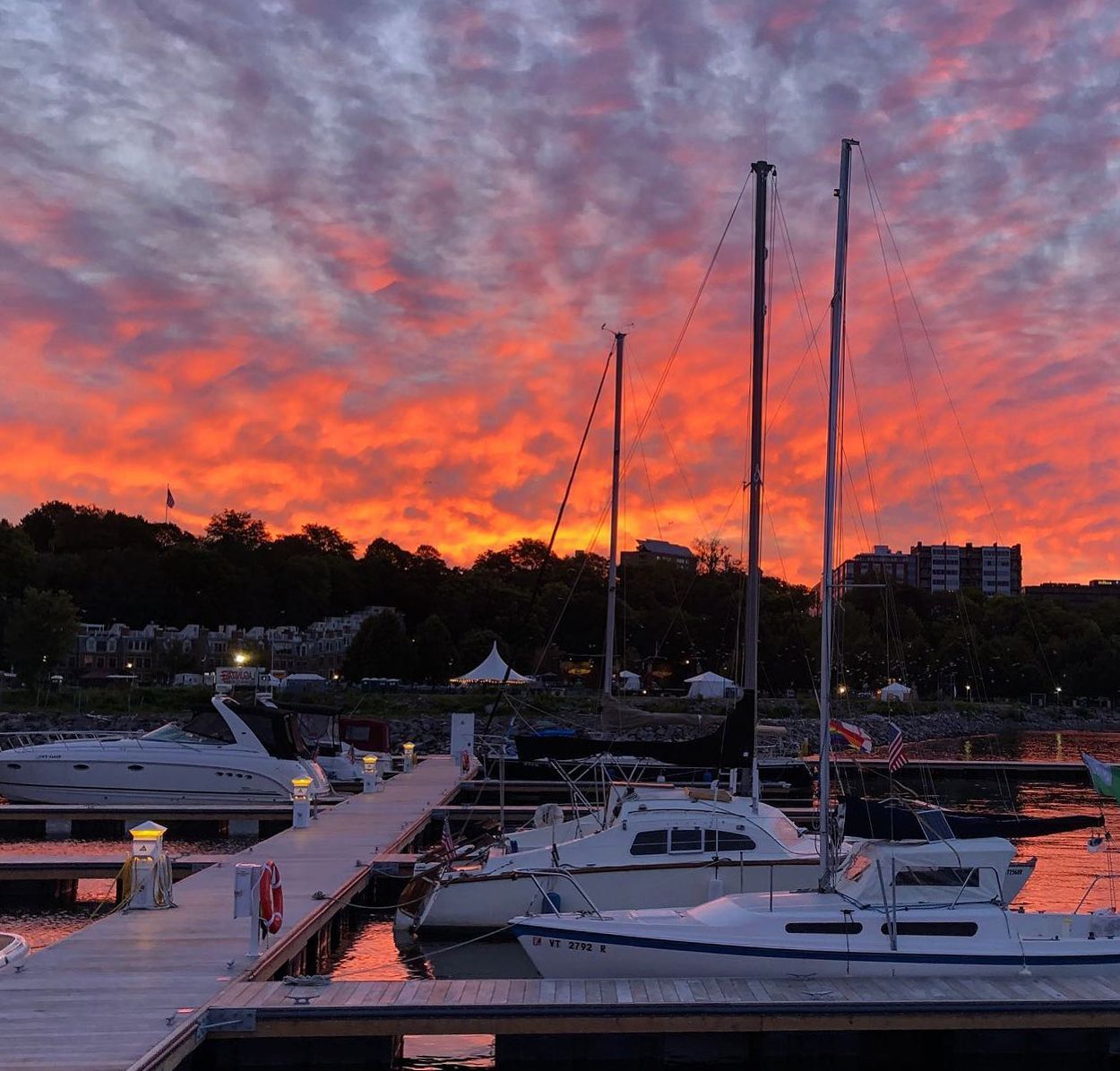 Fiery orange and purple sunset sky behind sailboat masts and a waterfront town