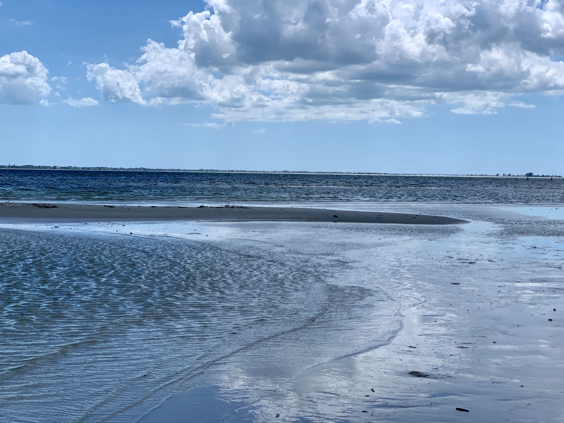 Sandy beach at low tide under a partly cloudy blue sky.