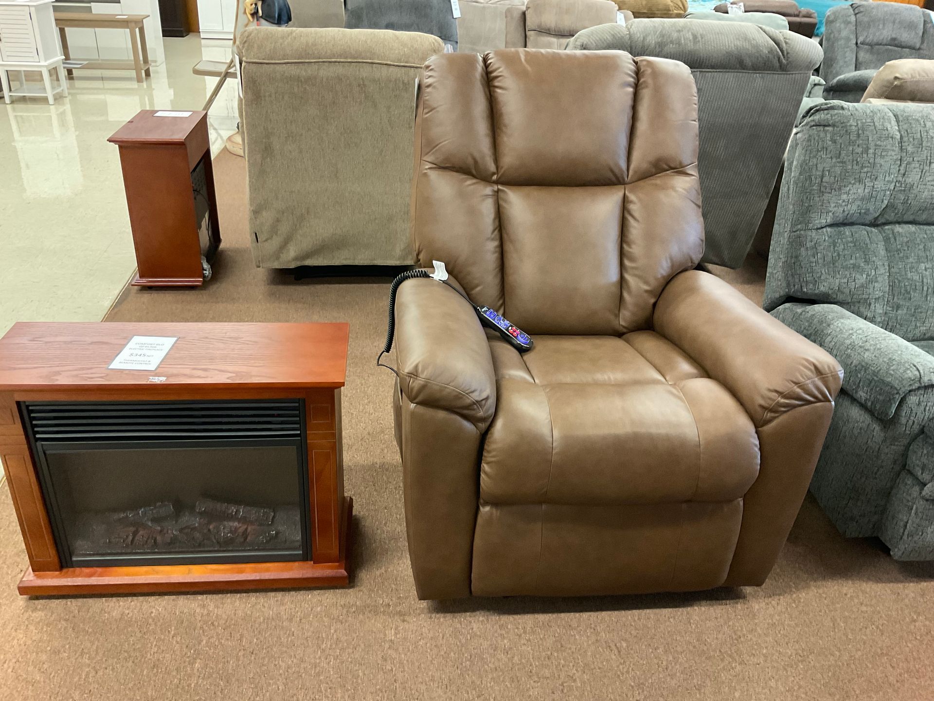 Brown recliner with remote, next to a fireplace unit, in a store setting.