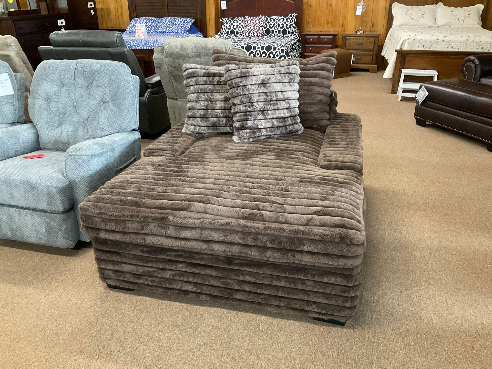 Brown textured chaise lounge with decorative pillows in a furniture store.