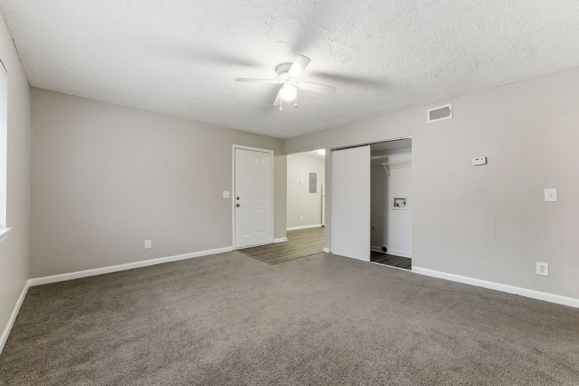 Empty carpeted bedroom with gray walls, ceiling fan, and open closet doors