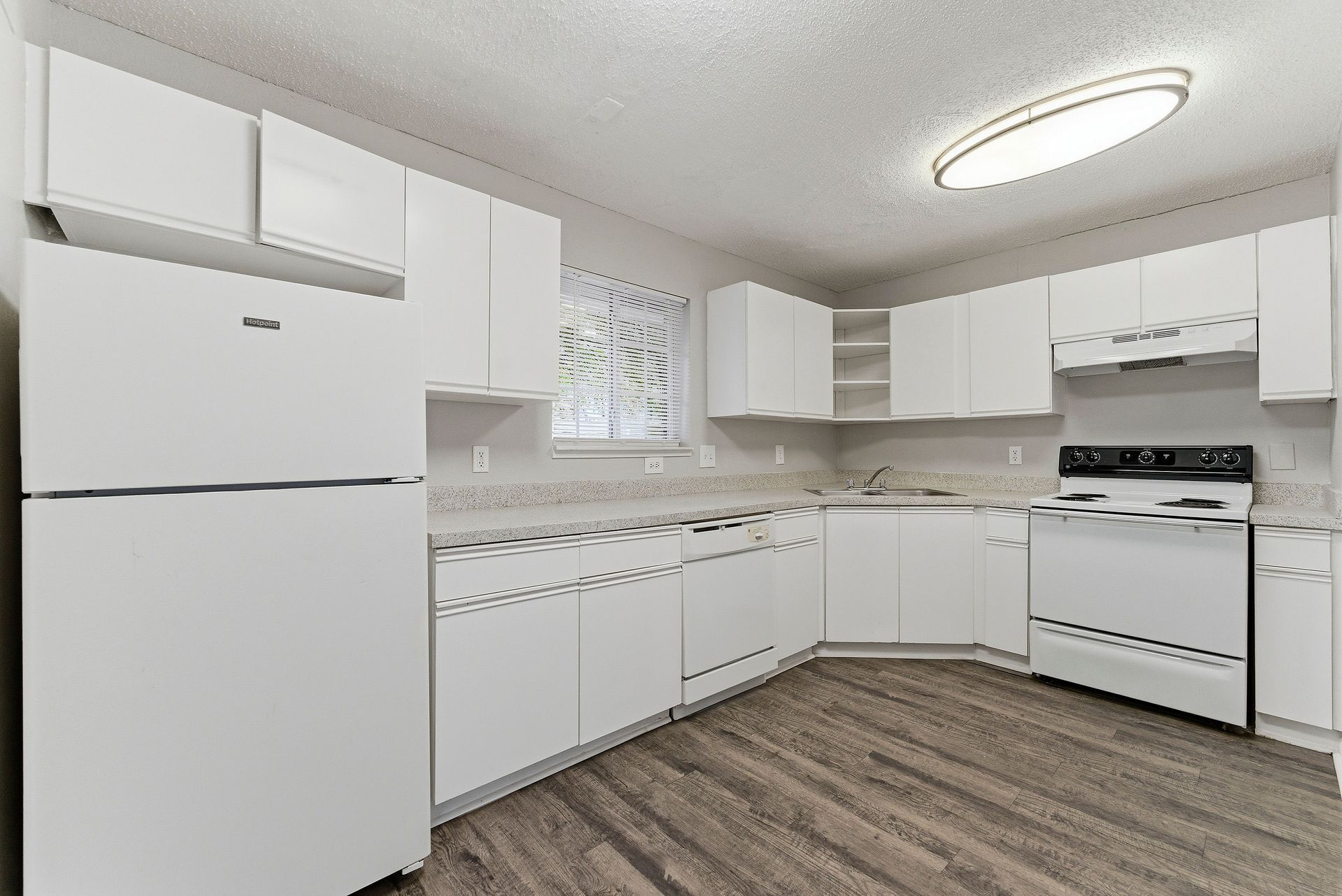 Bright white kitchen with cabinets, fridge, stove, and wood-look flooring