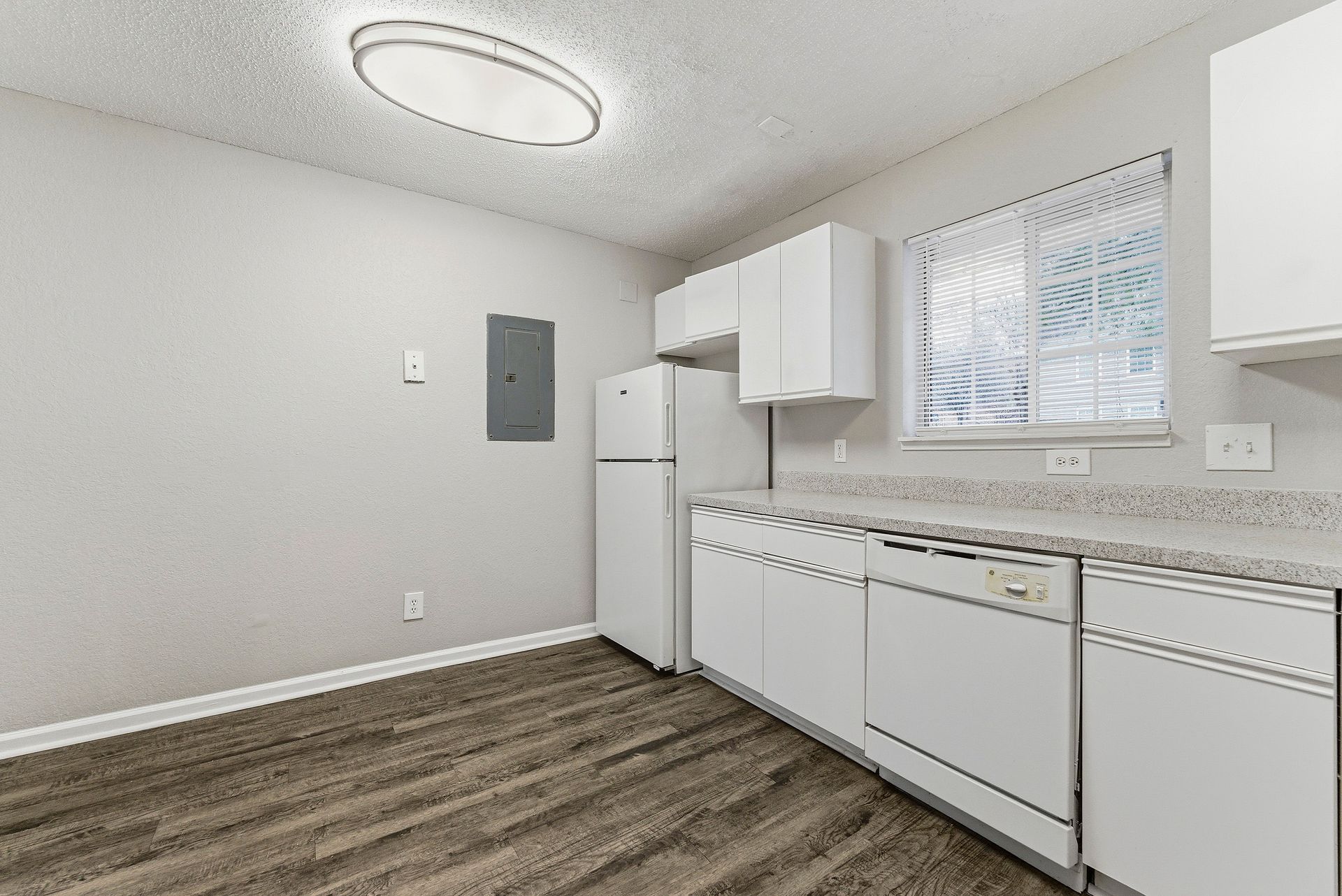 Empty white kitchen with white cabinets, refrigerator, dishwasher, and wood-look flooring