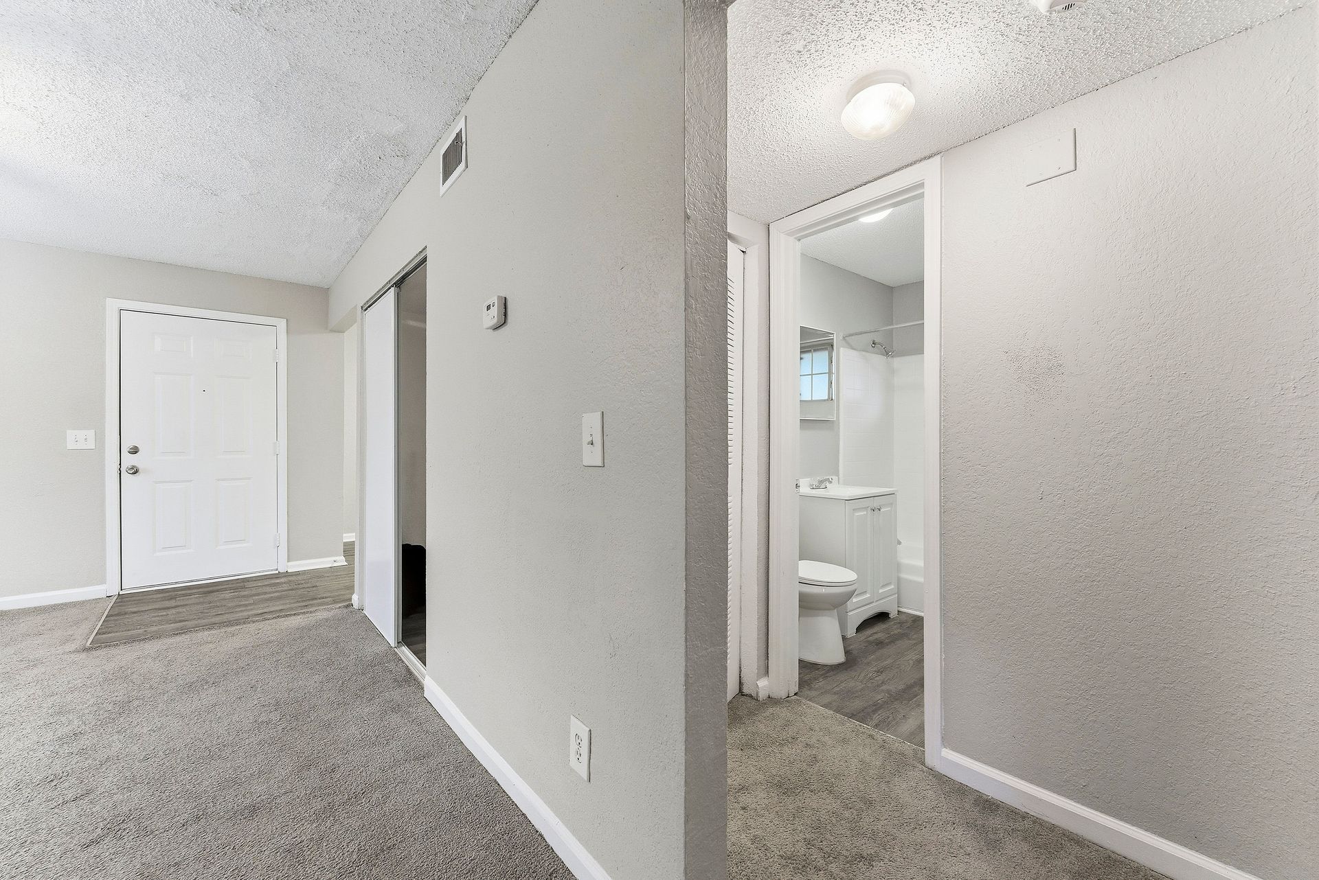 Empty carpeted hallway with light gray walls and a bathroom visible through an open doorway.