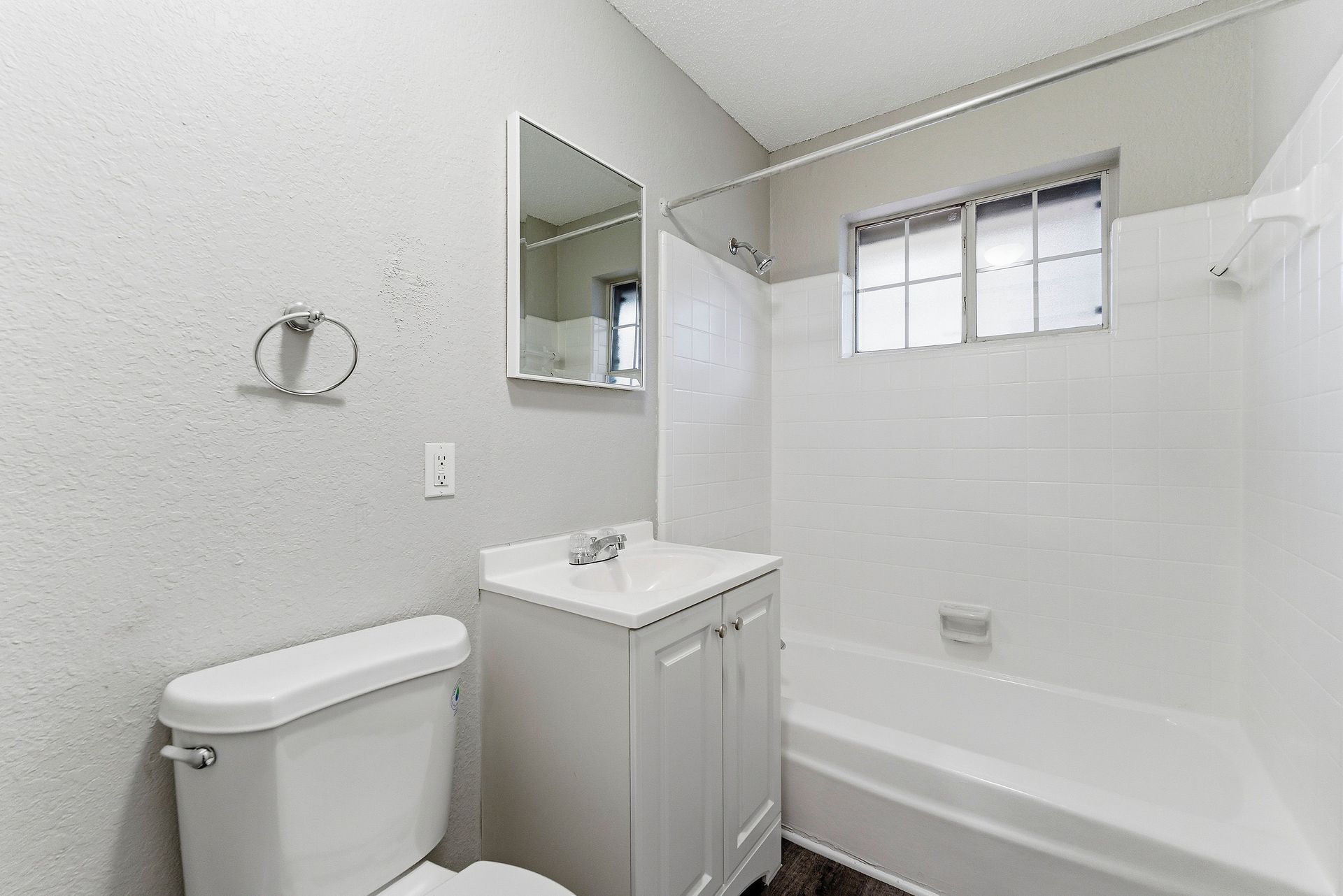 Small white bathroom with toilet, sink vanity, tub, mirror, and frosted window.