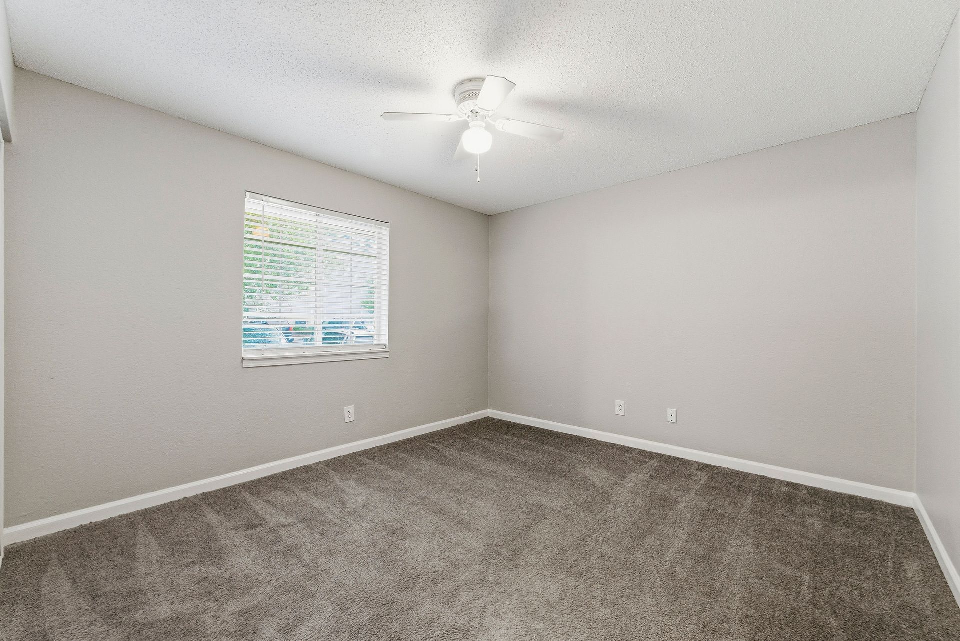 Empty beige bedroom with gray carpet, window blinds, and ceiling fan indoors