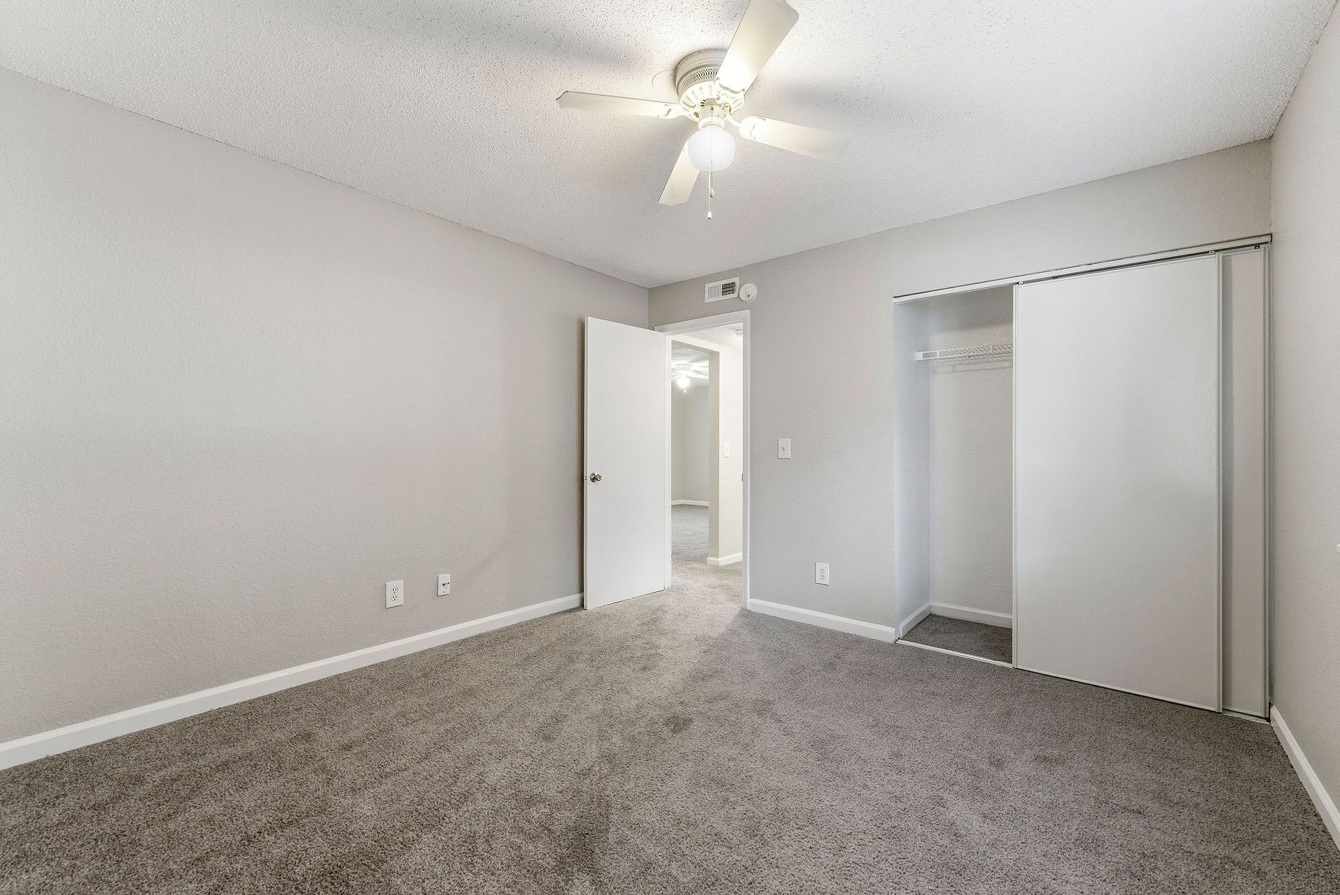Empty gray bedroom with carpet, ceiling fan, open door, and closet.