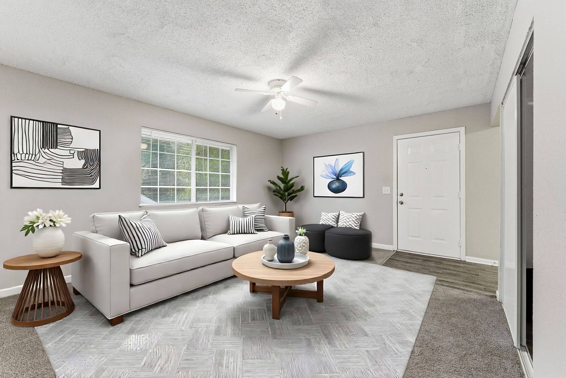 Bright living room with gray sofa, coffee table, wall art, and large window on a light carpet