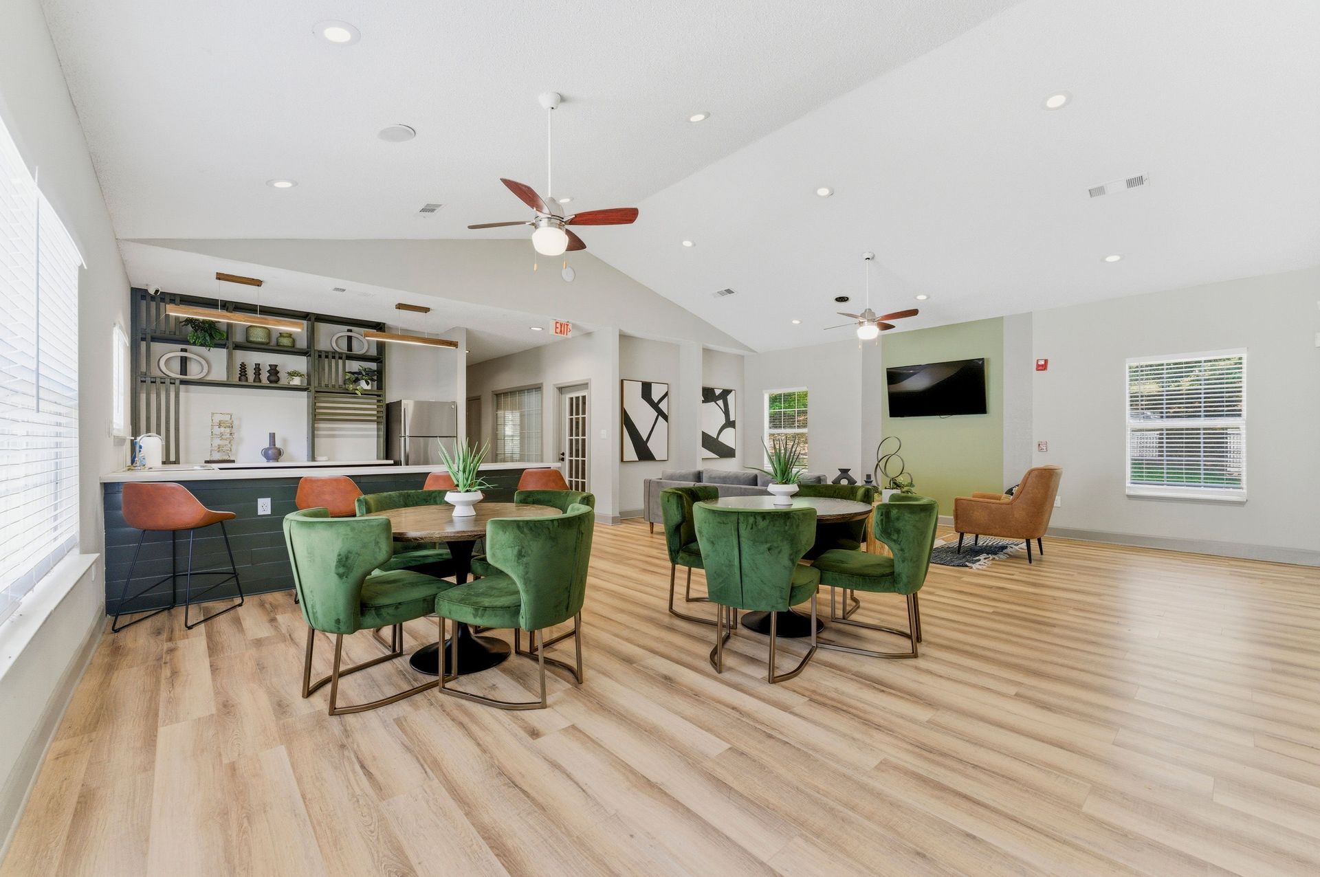 Bright modern lounge with green chairs, wooden tables, a bar, and ceiling fans in a spacious room