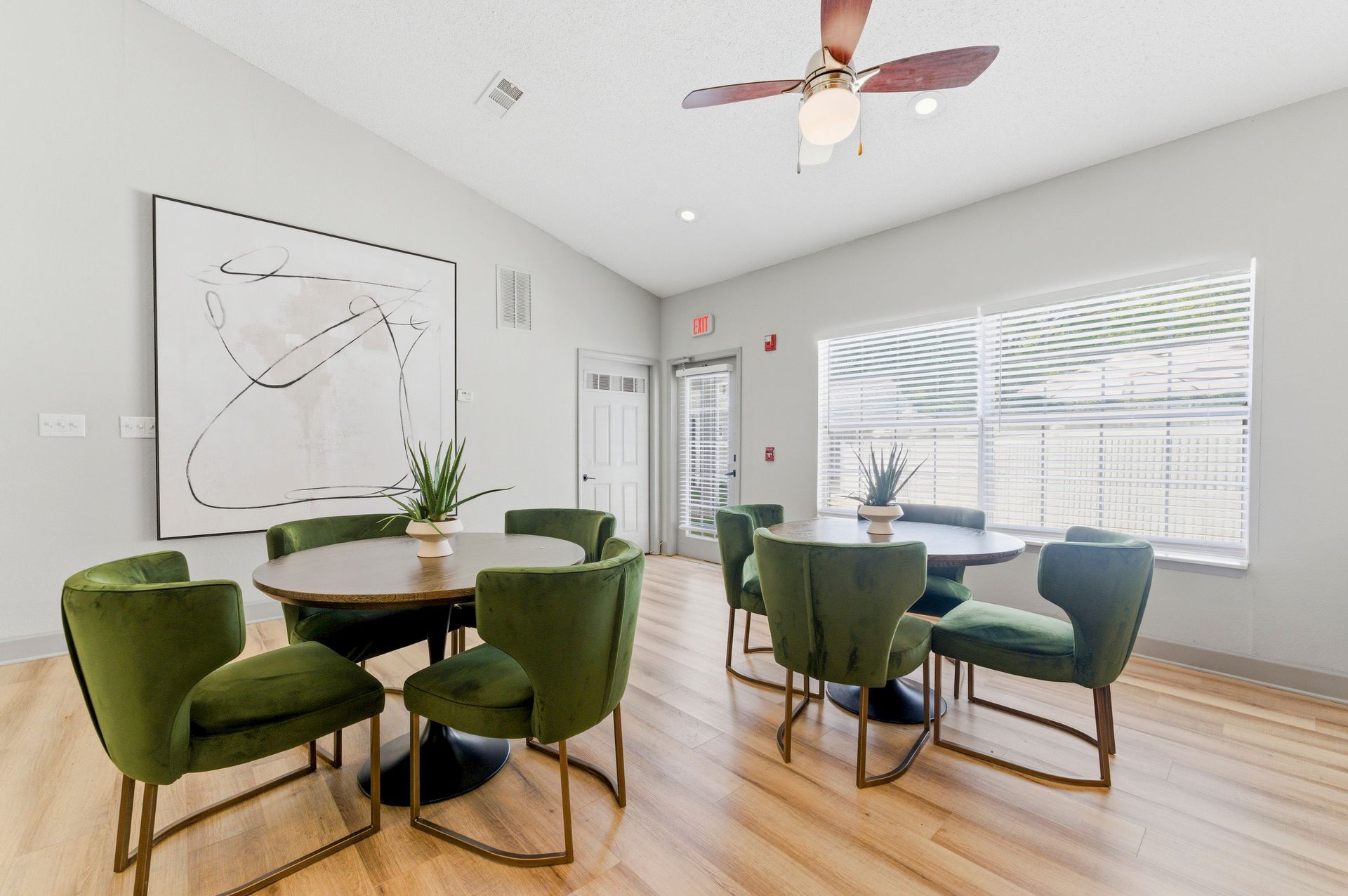 Modern dining room with round tables, green chairs, large windows, and a ceiling fan