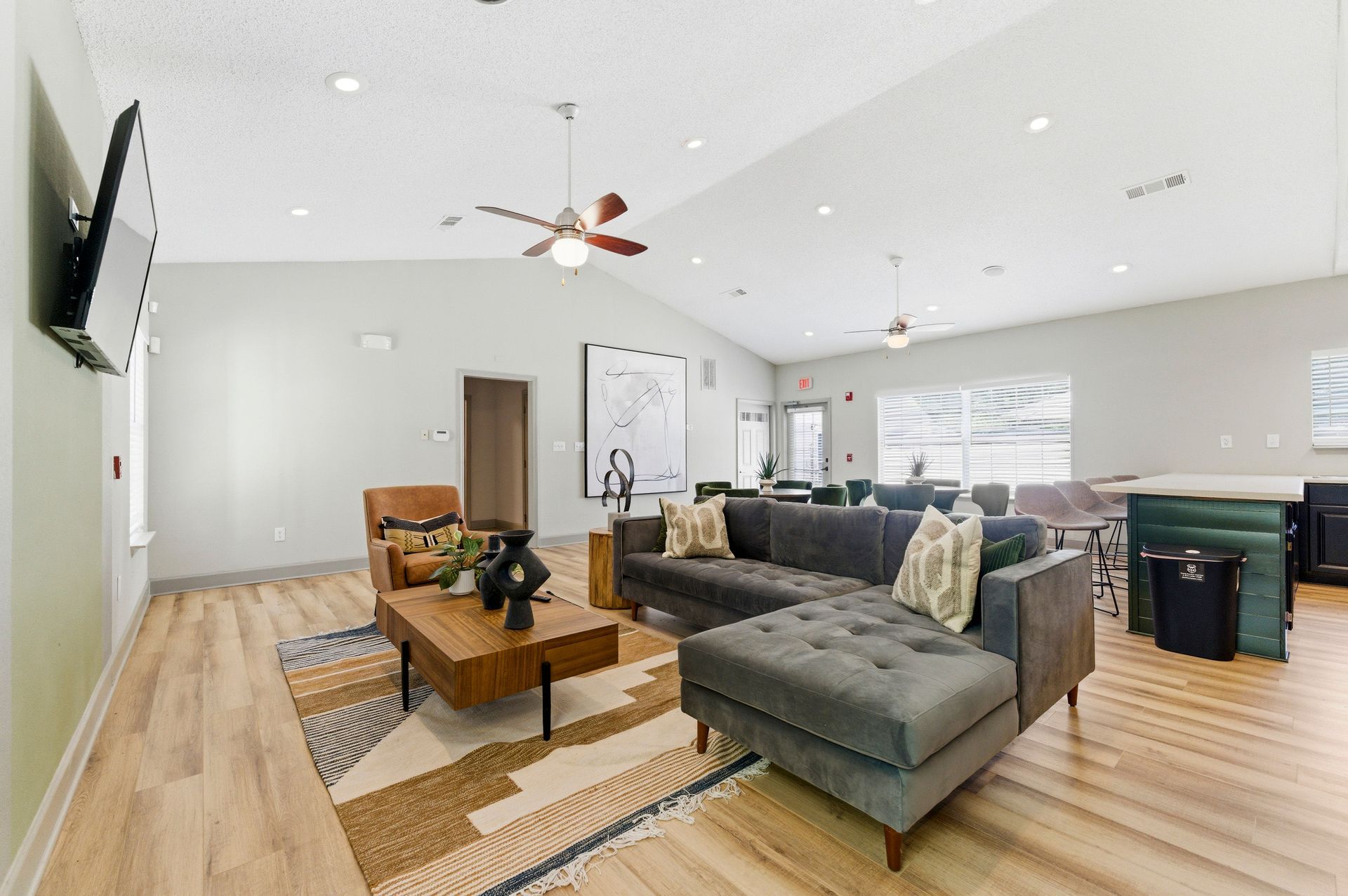 Bright living room with gray sectional, wooden coffee table, TV, and kitchen island in the background