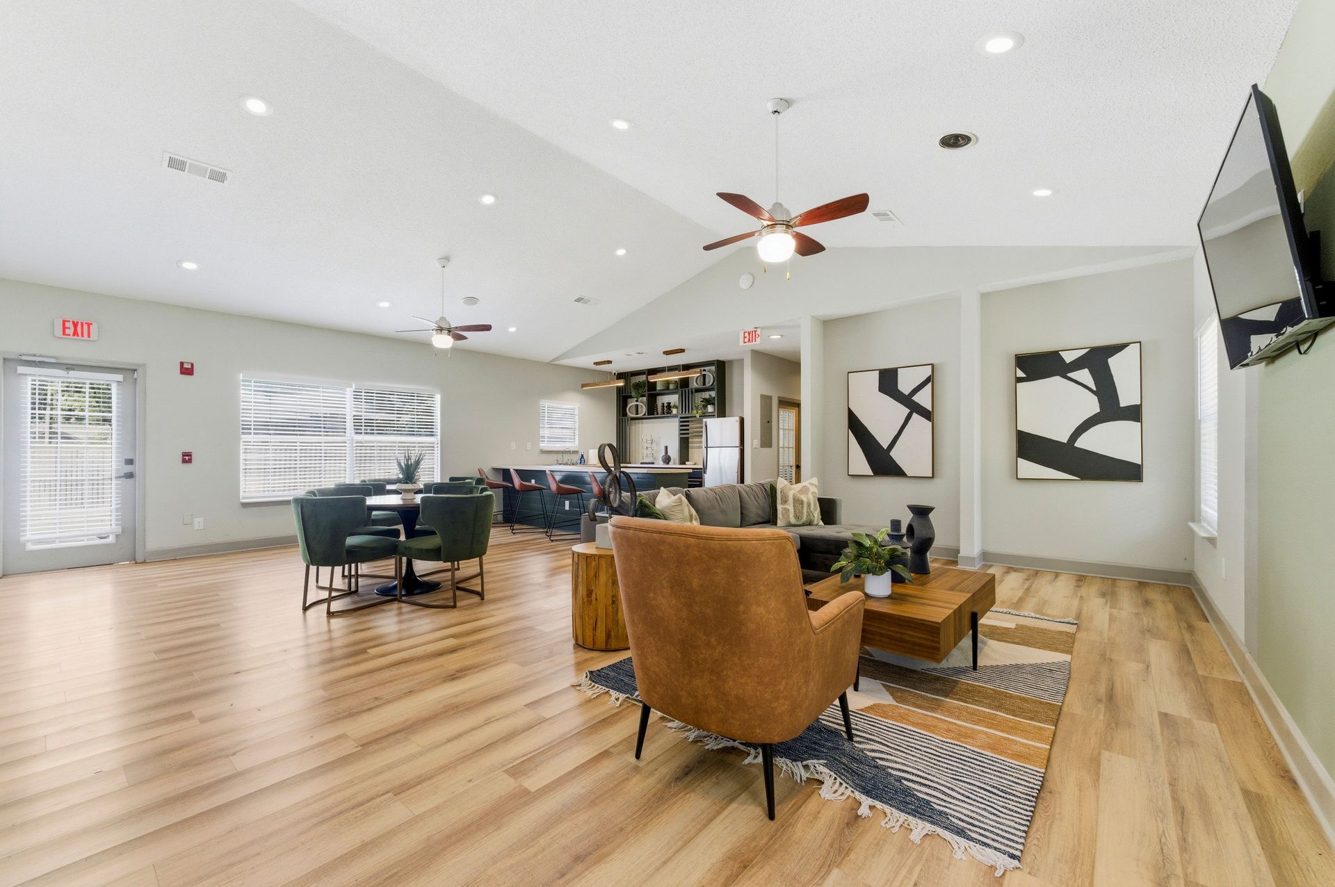 Bright open living room with wood floors, tan chairs, gray walls, and a wall-mounted TV.