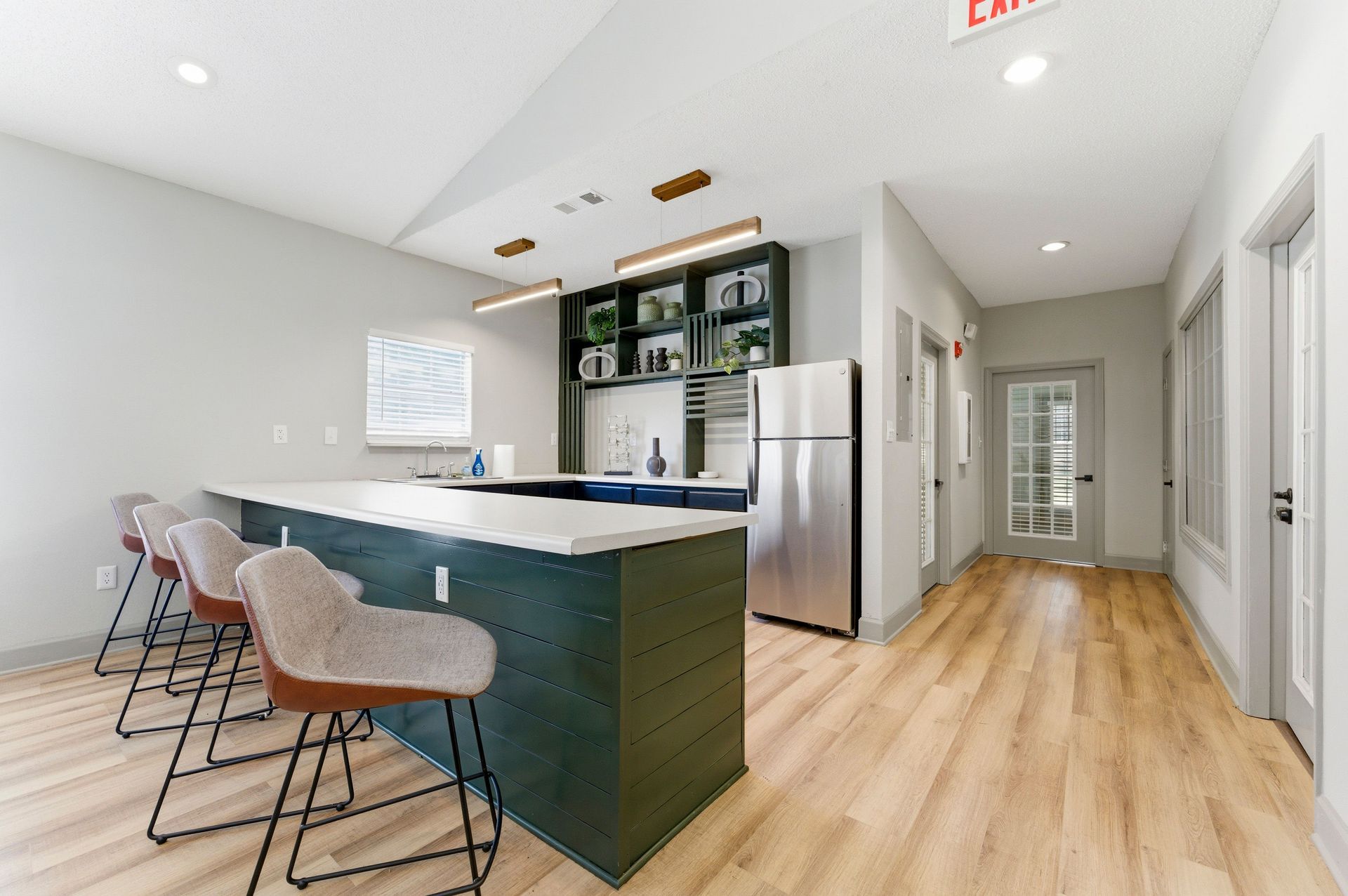 Modern kitchen with teal island, pink stools, stainless fridge, and light wood floors