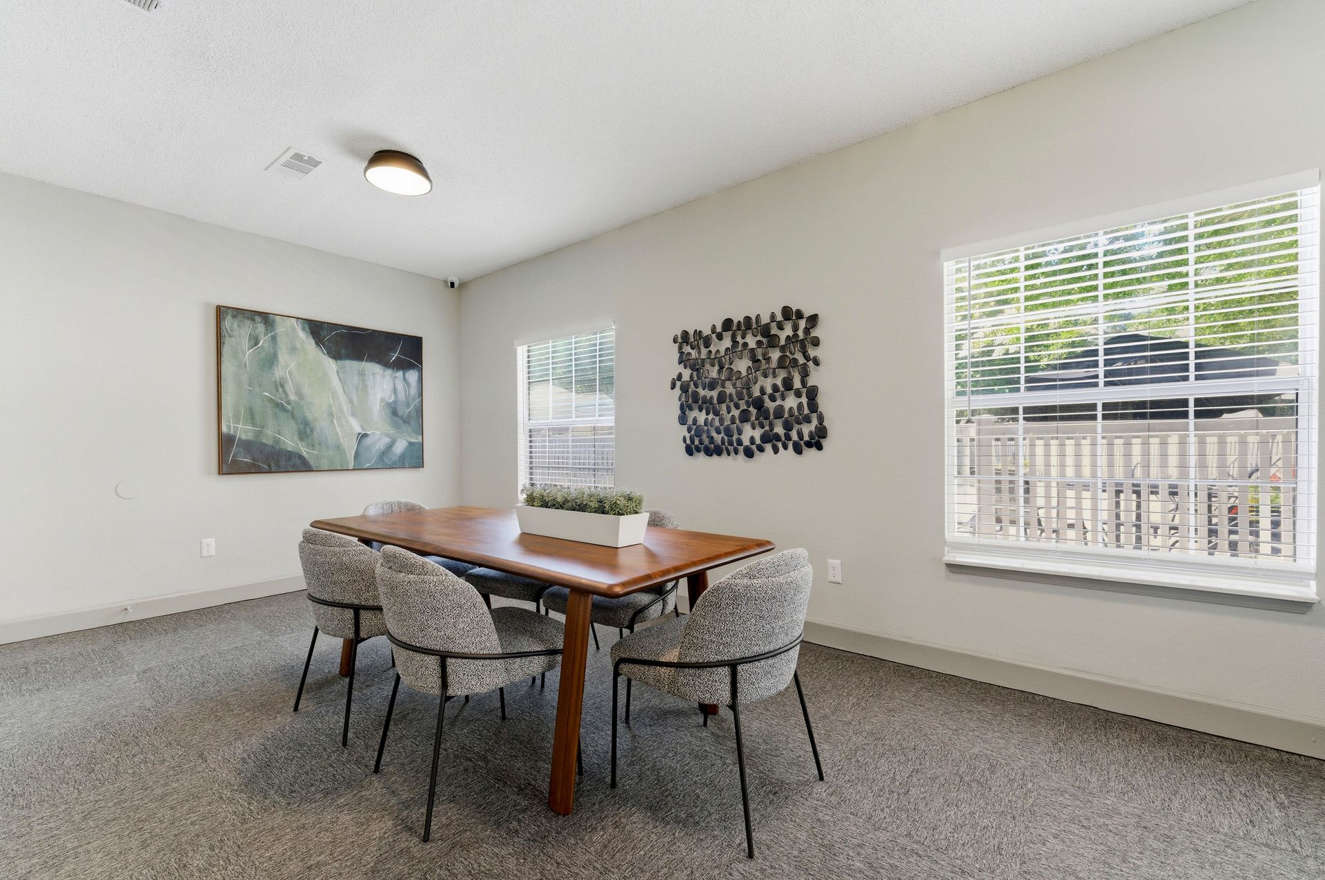 Minimal dining room with wooden table, four chairs, wall art, and large windows with blinds.