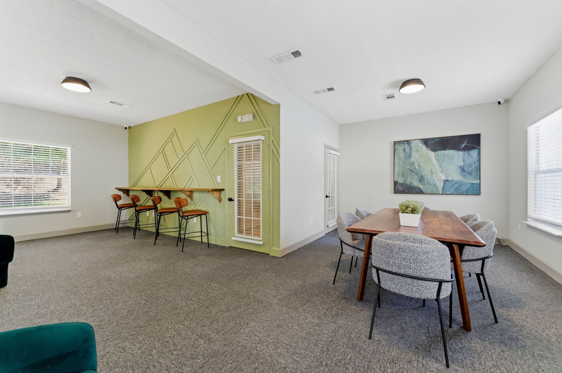 Open living/dining room with green accent wall, wooden table, chairs, and carpeted floor