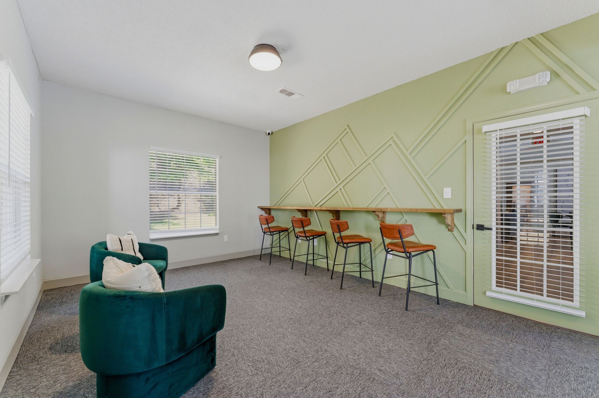 Cozy room with green accent wall, teal chair, bar stools, and tall window blinds.
