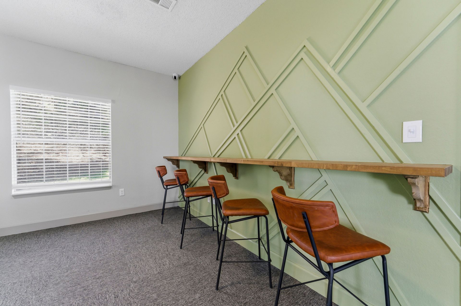 Small meeting room with green accent wall, long counter, and four orange stools on carpeted floor