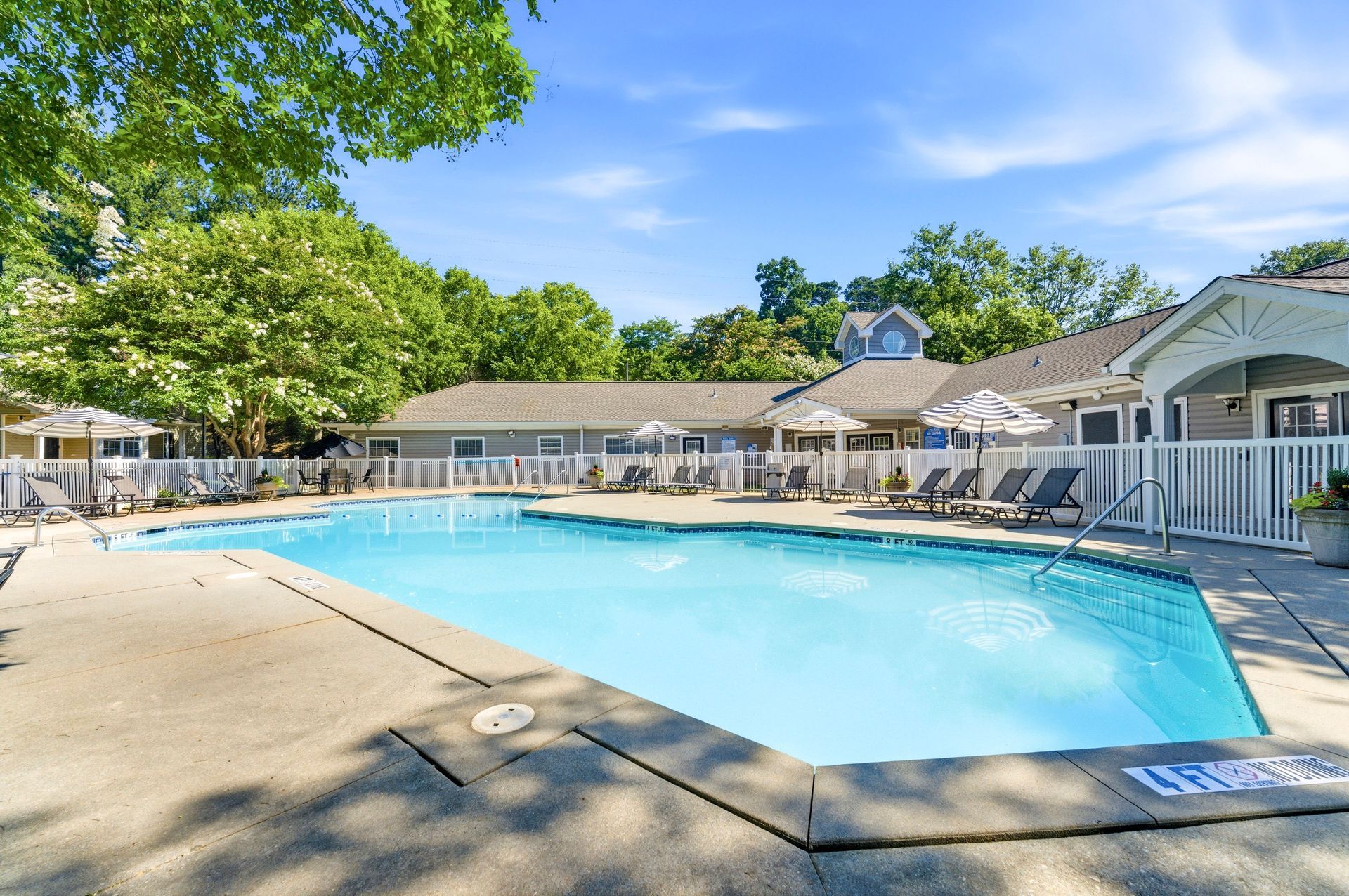 Outdoor swimming pool with lounge chairs and umbrellas beside a clubhouse on a sunny day