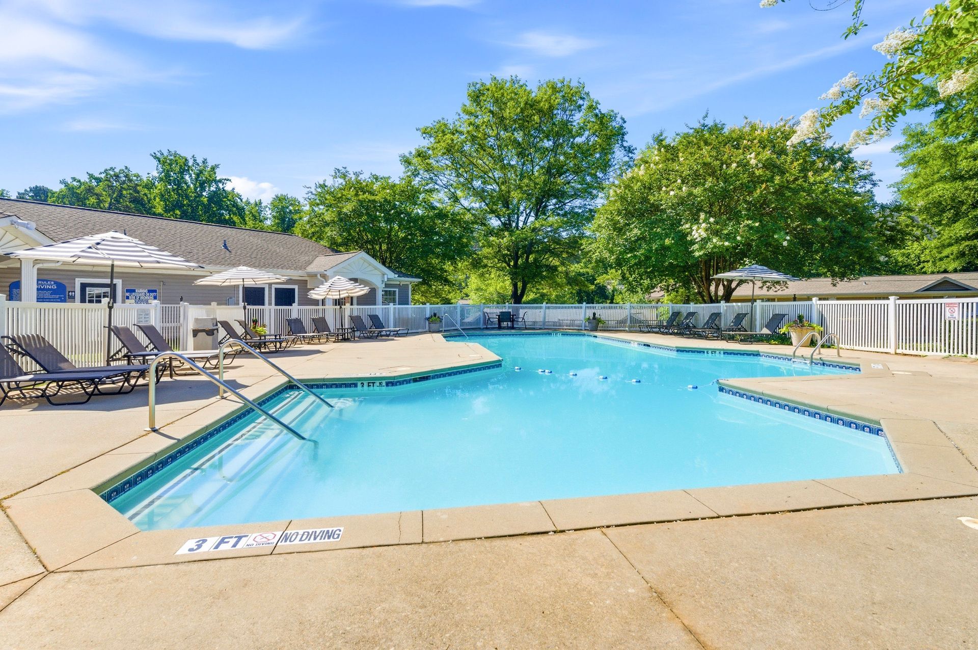 Outdoor resort swimming pool with lounge chairs, blue water, and white cabanas under a sunny sky
