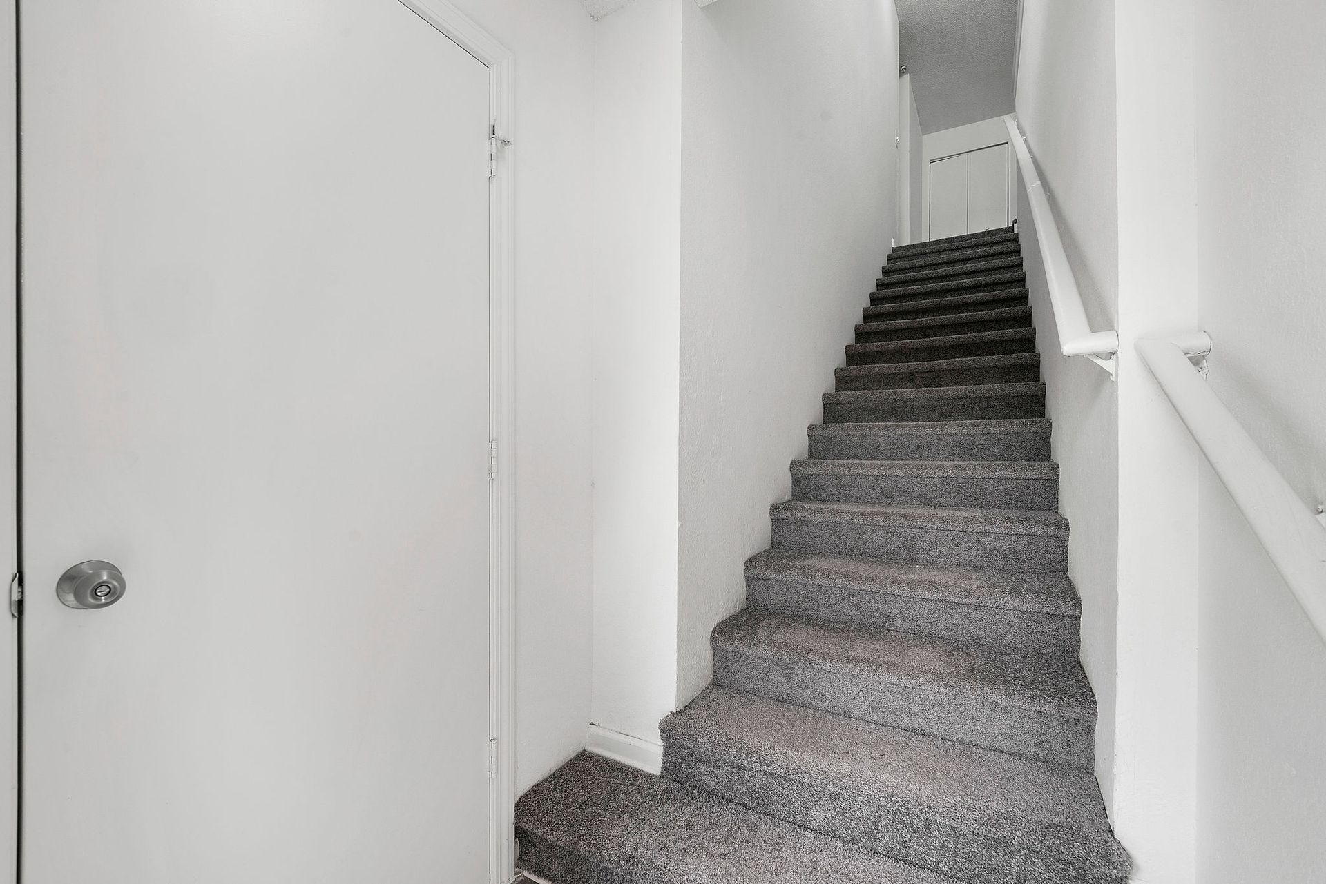 Narrow indoor stairway with carpeted steps and white walls beside a closed door.