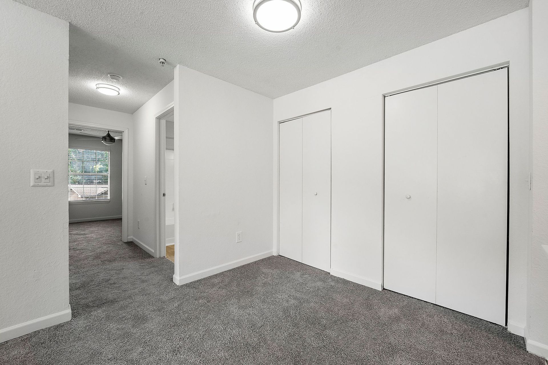 Empty carpeted hallway with white walls and closed closet doors, lit by a ceiling light.