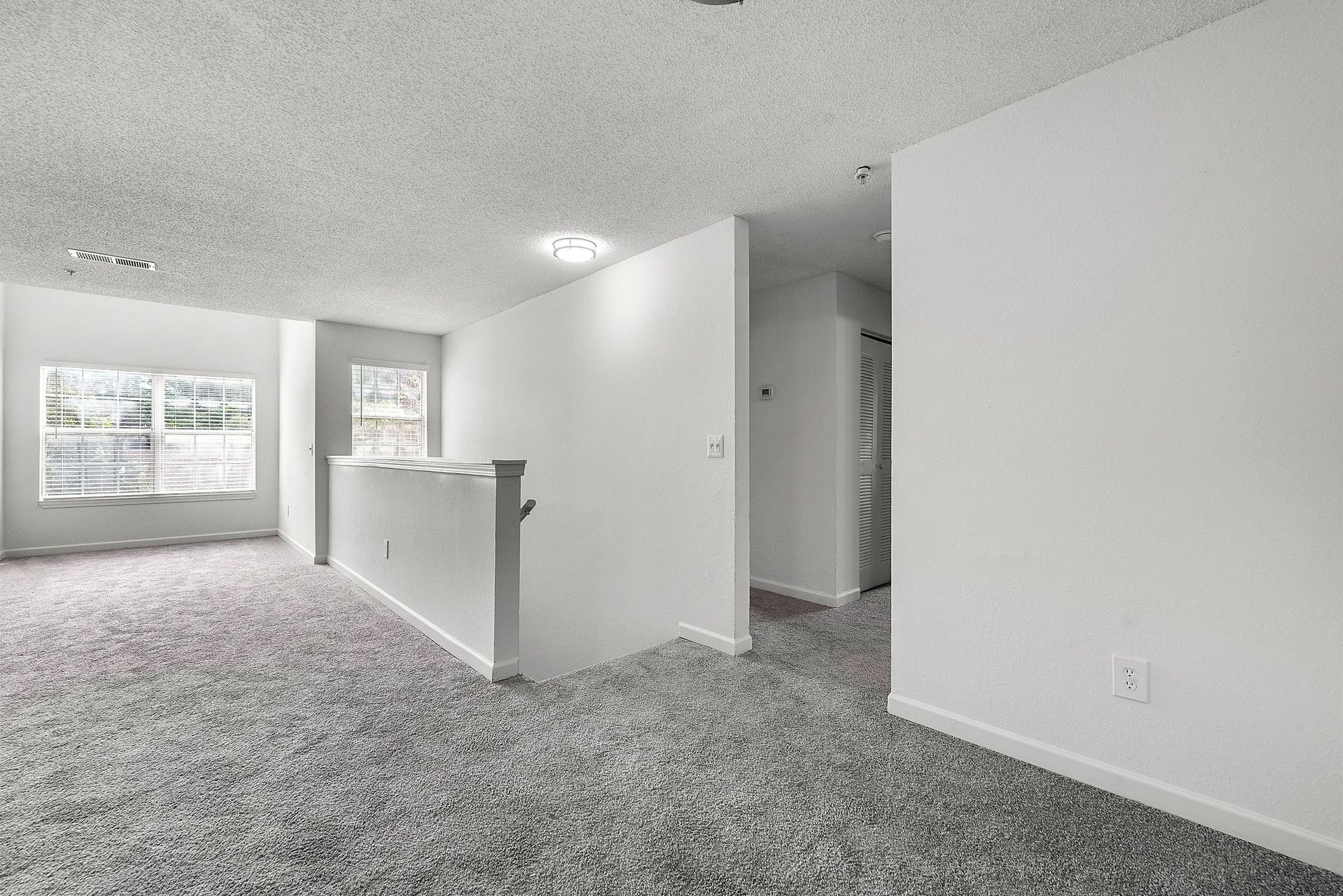 Empty carpeted living room with white walls, a half wall, and windows letting in daylight.