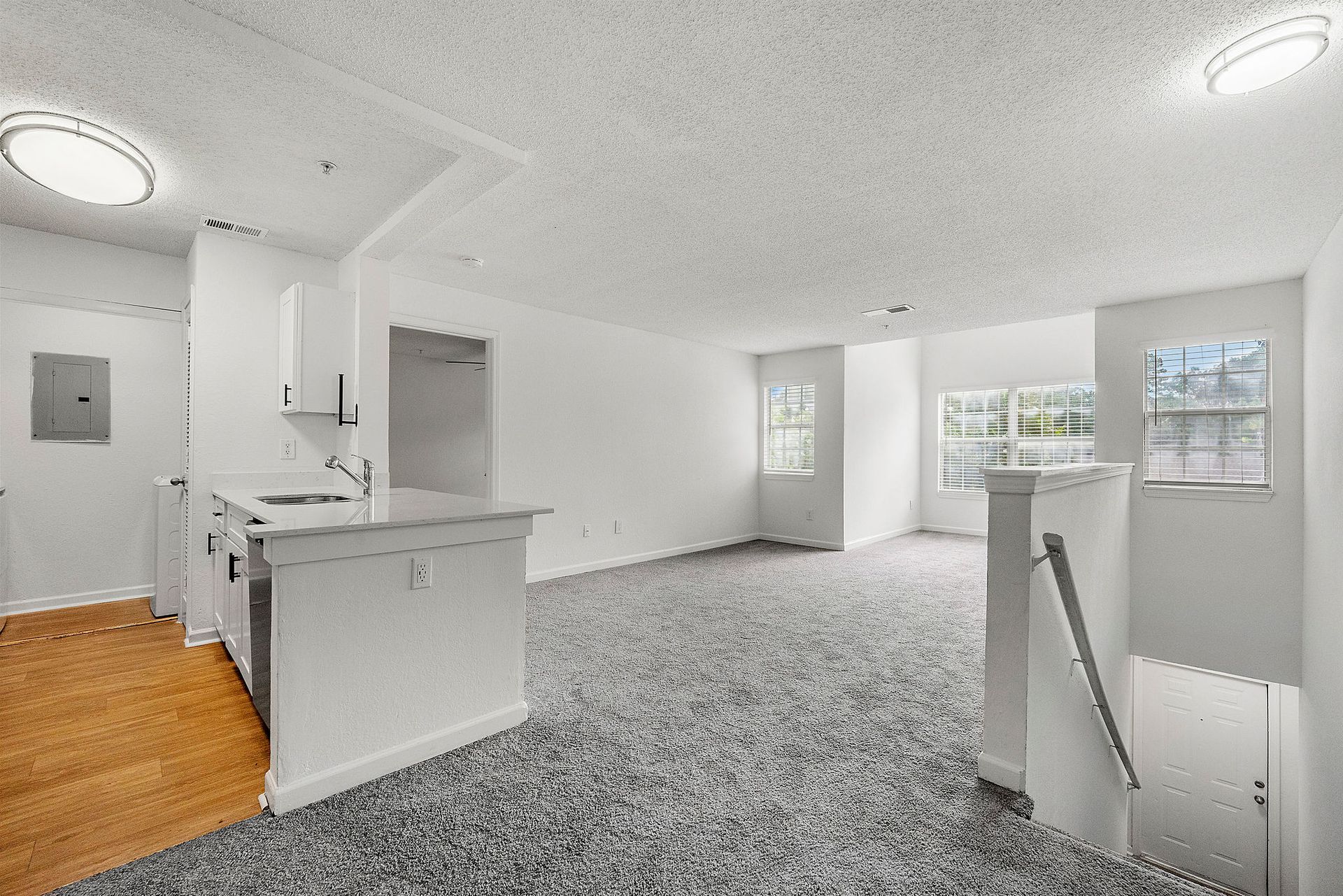 Empty bright living room with gray carpet, white walls, kitchen island, and large windows