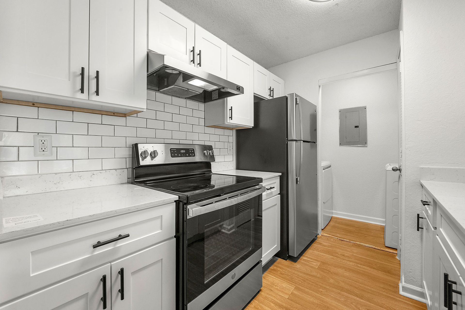 Modern white kitchen with stainless steel appliances, gray cabinets, and hardwood floor