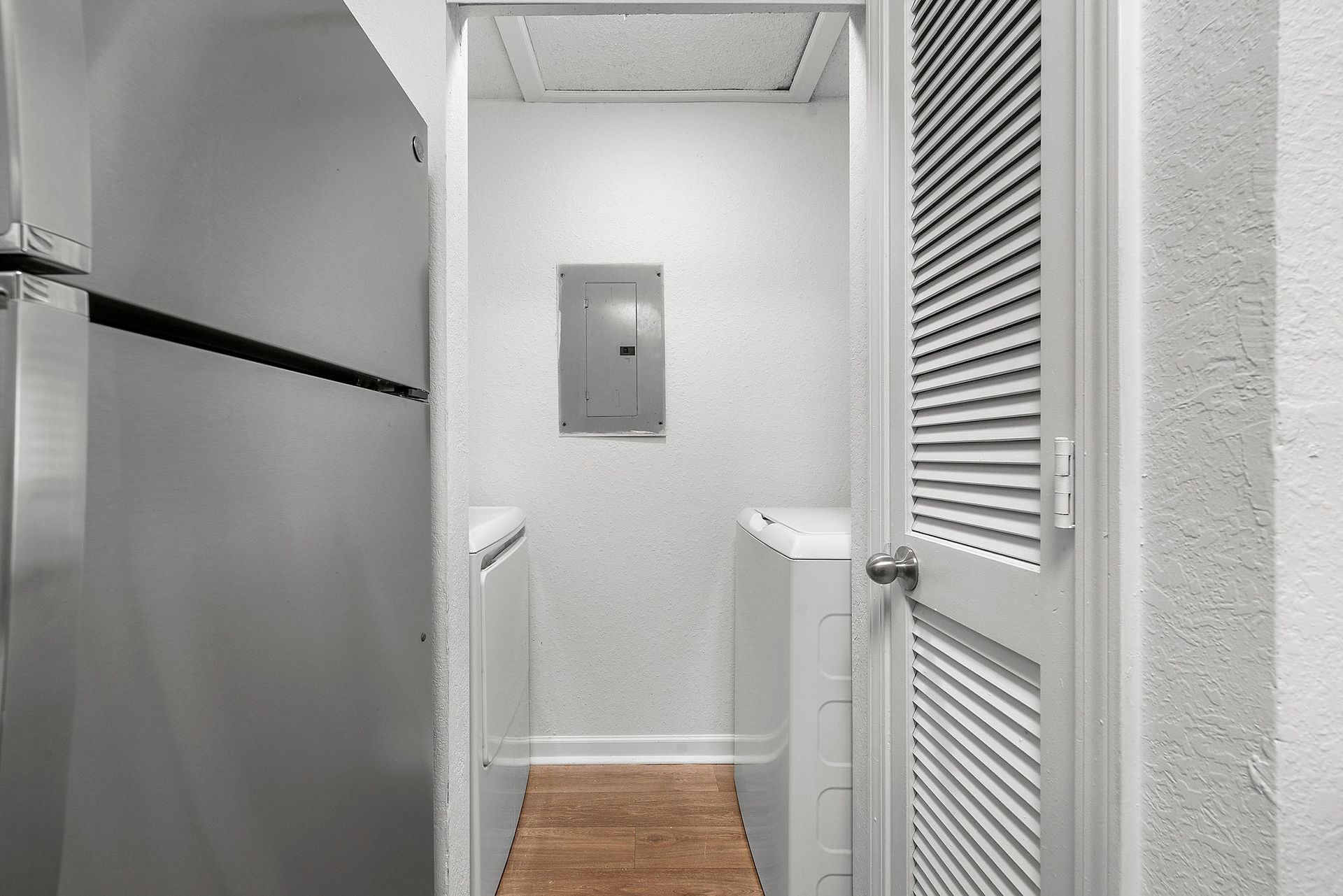 Narrow white hallway with a refrigerator on the left, louvered doors on the right, and a wall panel ahead.