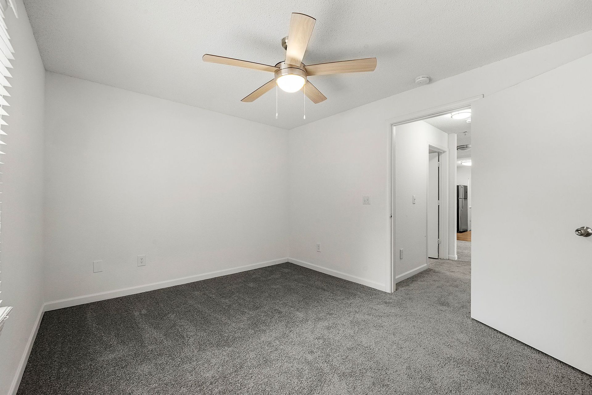 Empty white bedroom with gray carpet and a ceiling fan, viewed from the doorway