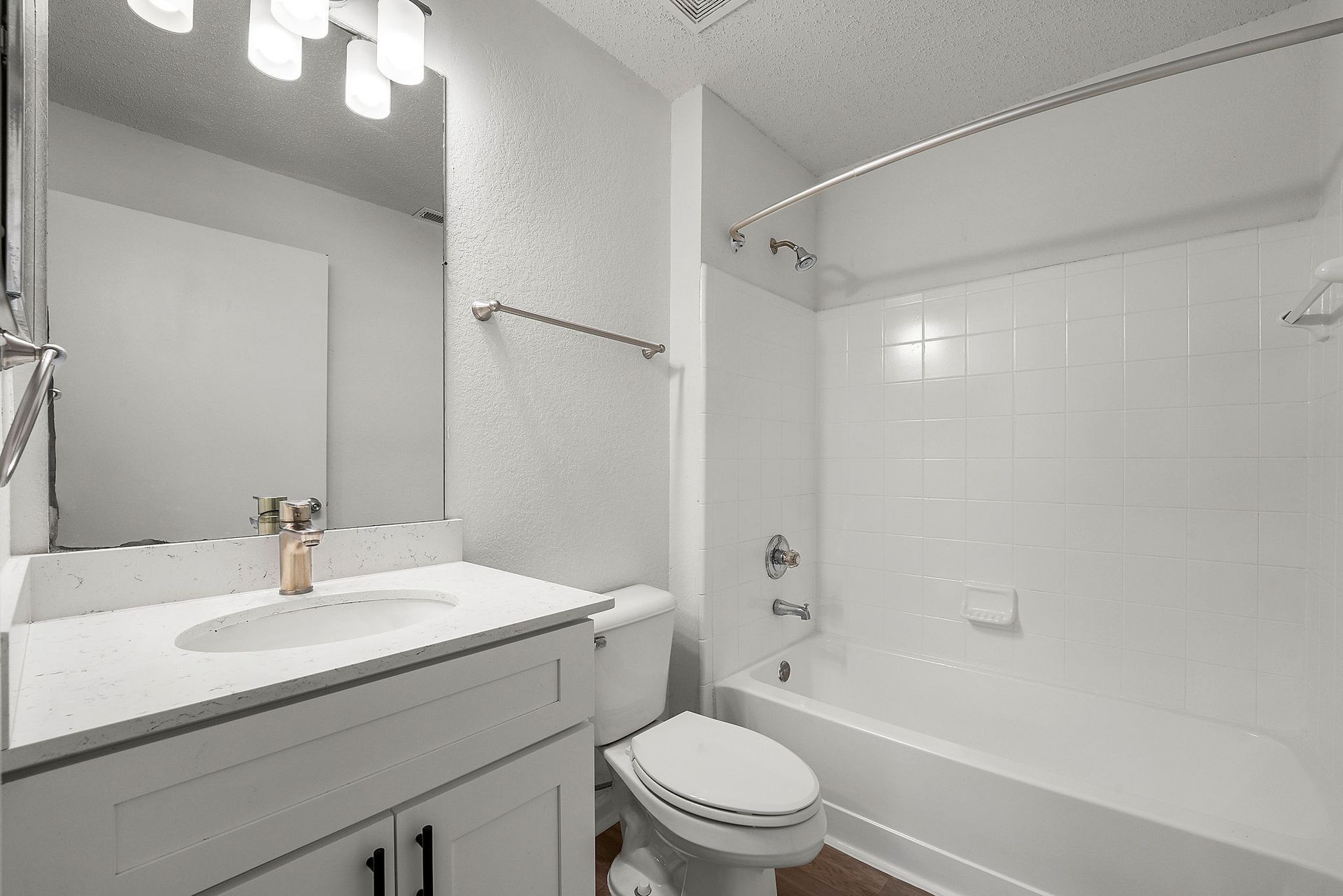 Bright white bathroom with vanity, sink, mirror, toilet, and bathtub/shower combo.